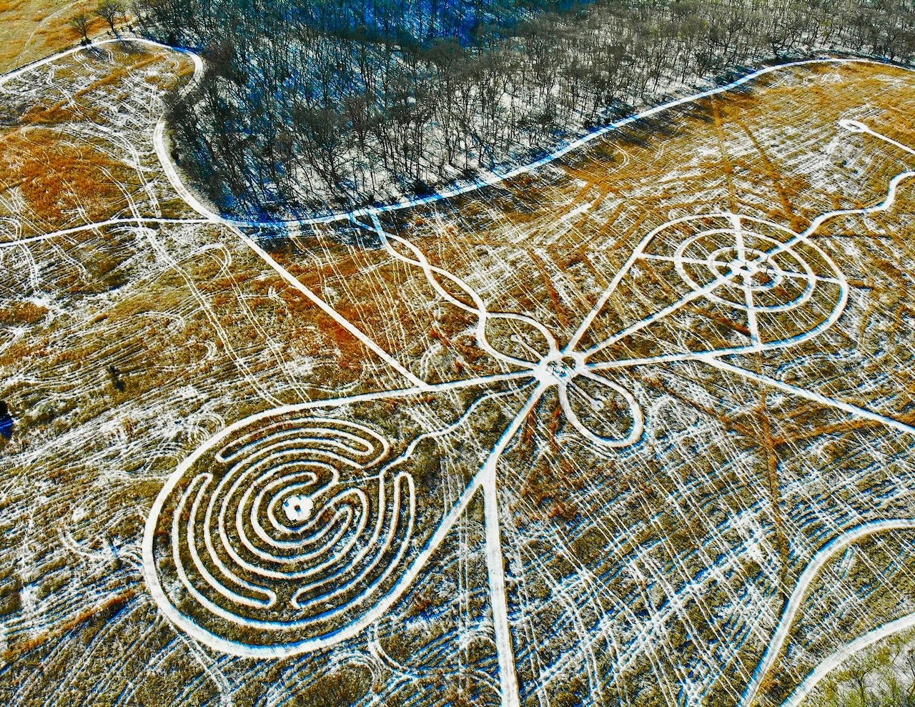 Aerial view of large white geoglyphs on a brown landscape with roads and fields, forming spiral and geometric patterns.