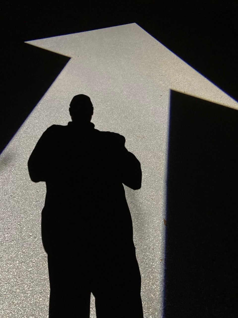 Silhouette of a person standing in front of a large, illuminated arrow pointing upward, against a dark background.