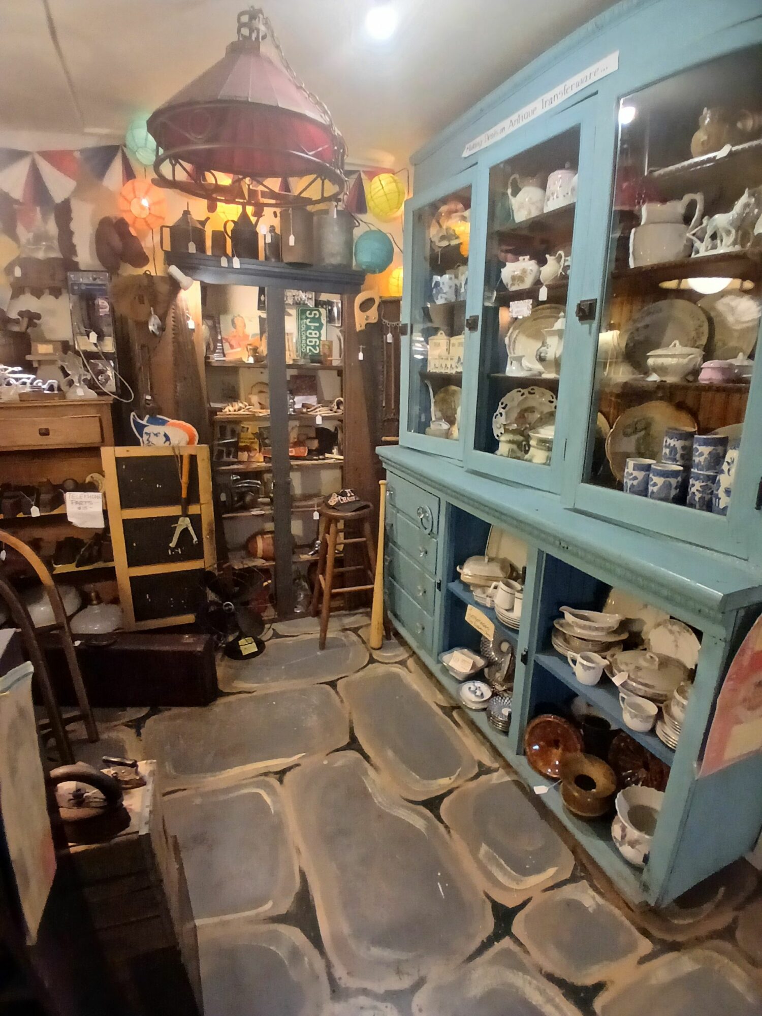 Room with display cabinet filled with various objects, wooden furniture, and a stone floor.