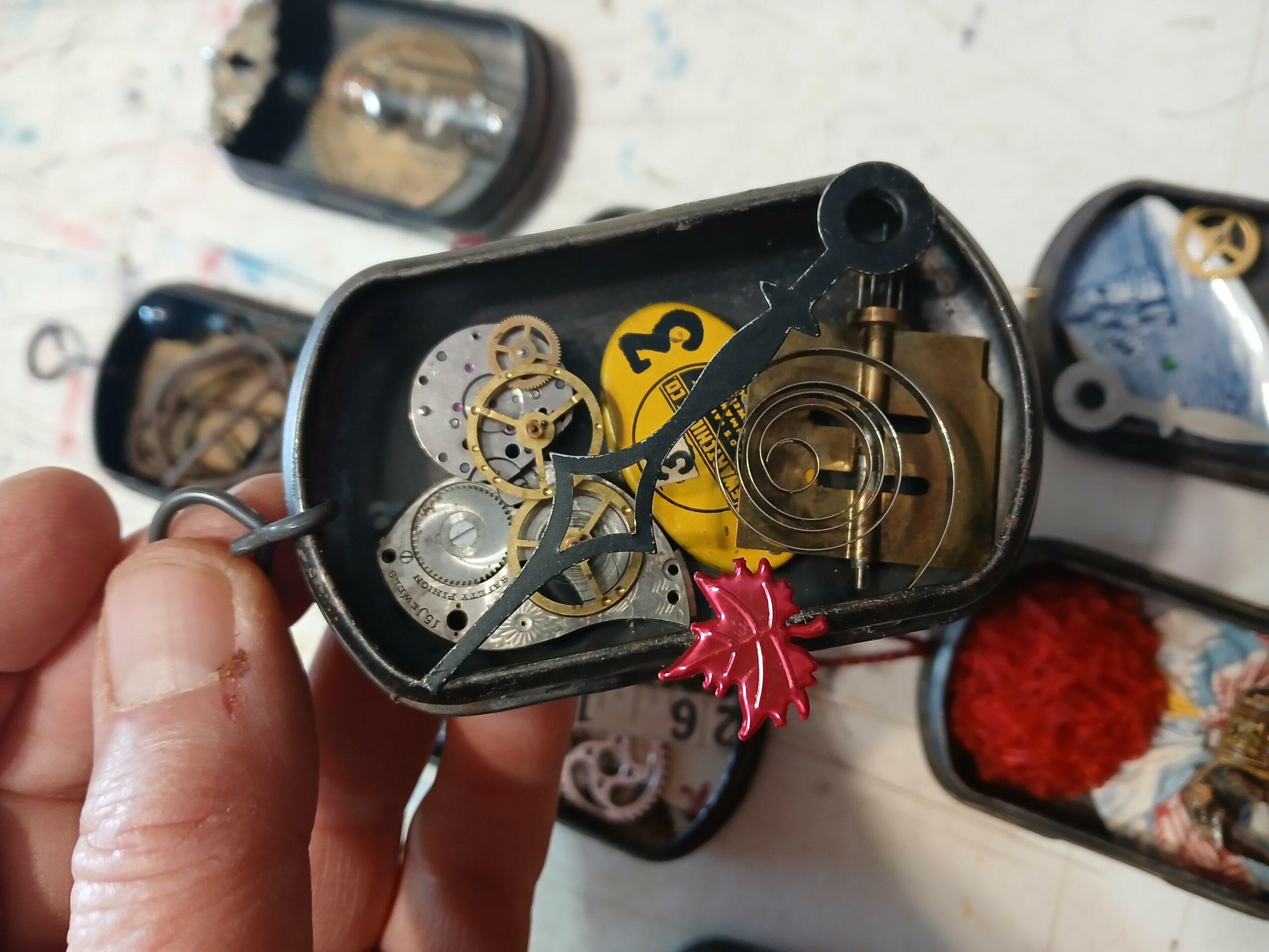 Open watch case showing gears and mechanical components inside, with a hand holding it. Background includes other watch parts and tools.