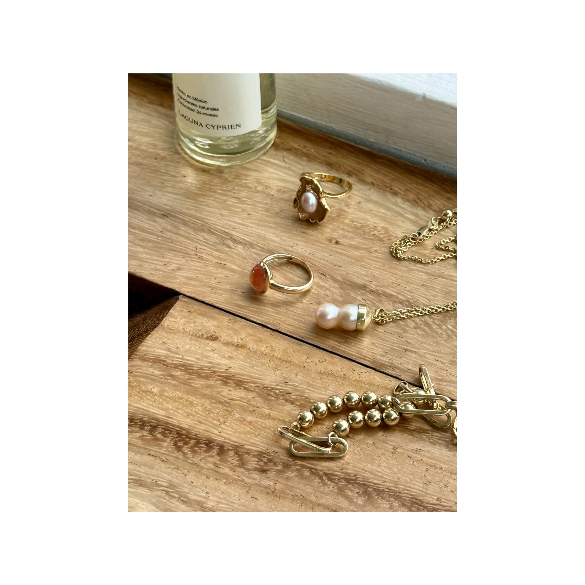 Jewelry and a bottle on a wooden surface, including a ring, earrings, a necklace, and a bracelet.