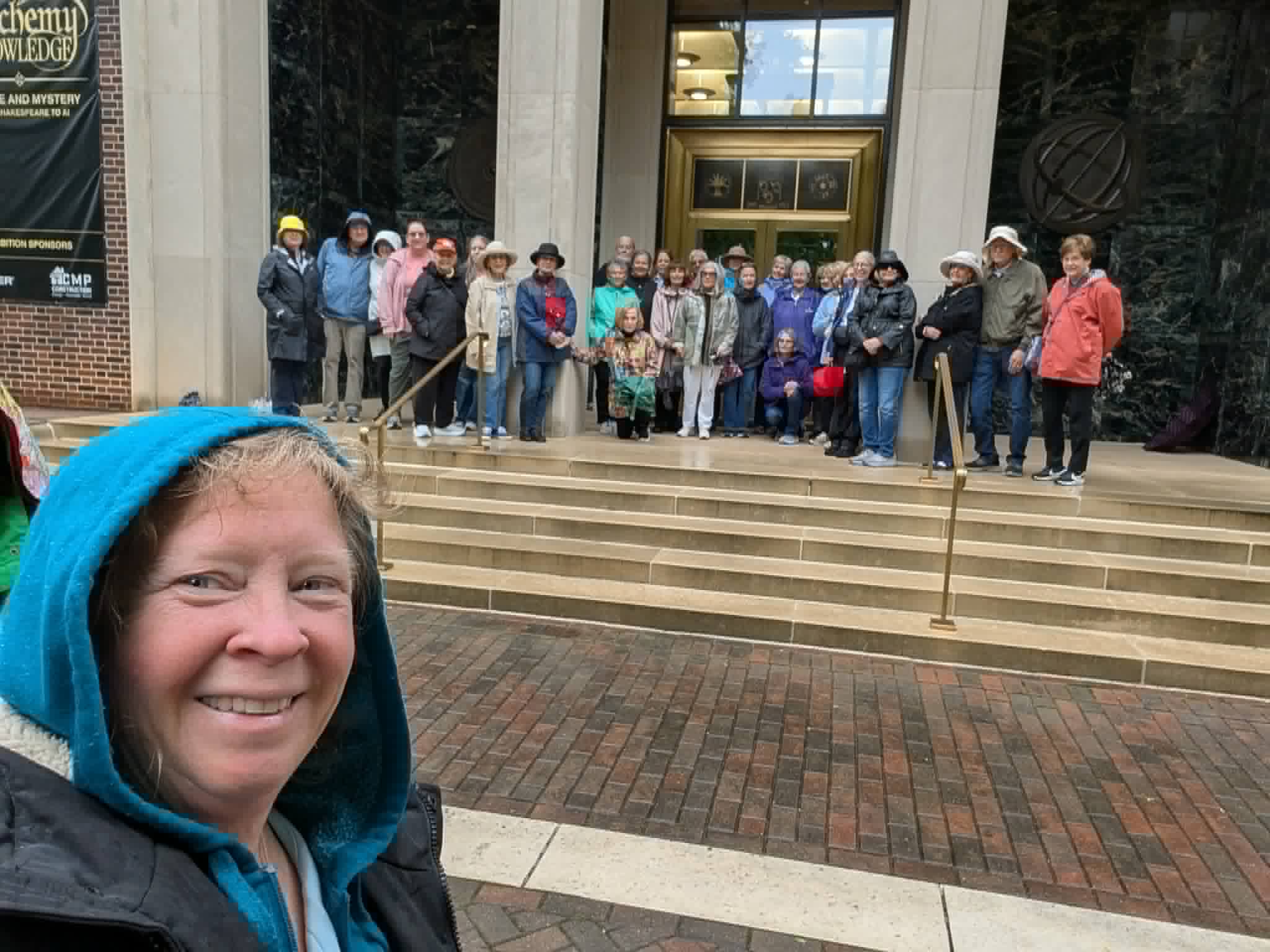 Woman smiling in foreground with a group of people standing on steps in background outside a building.