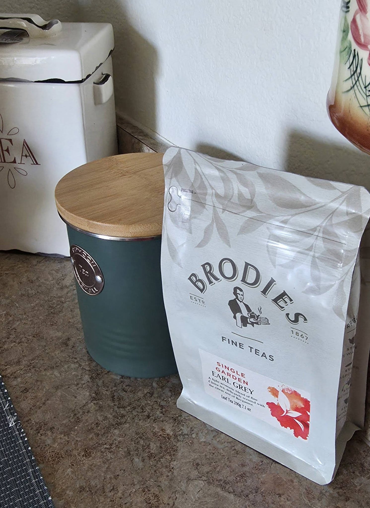 Bag of Brodies fine teas leaning against a teal container with a wooden lid, on a kitchen countertop.