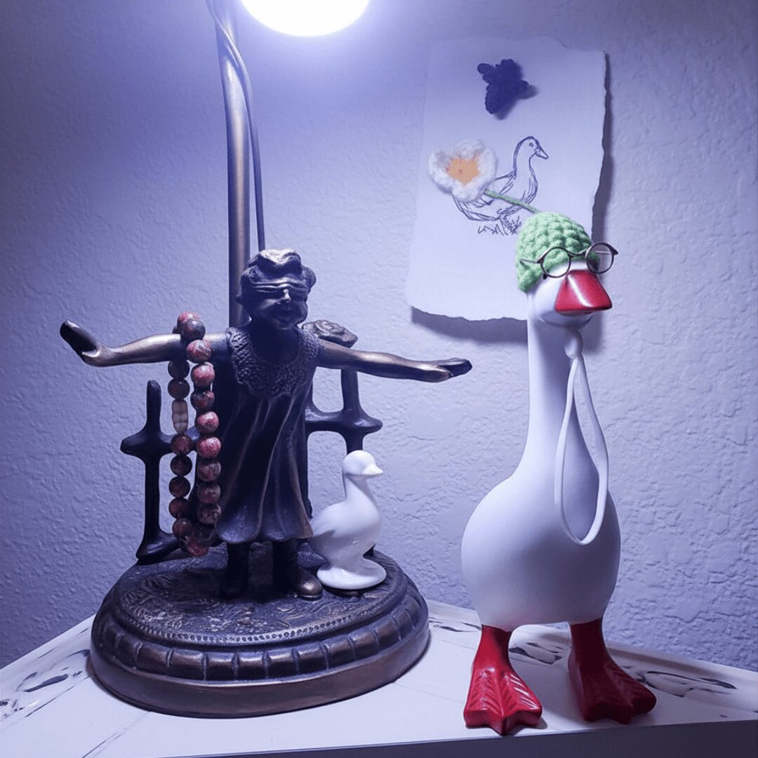 Decorative figurines of a dog with a beaded necklace and a tall white bird with red feet and a green hat, on a white surface.