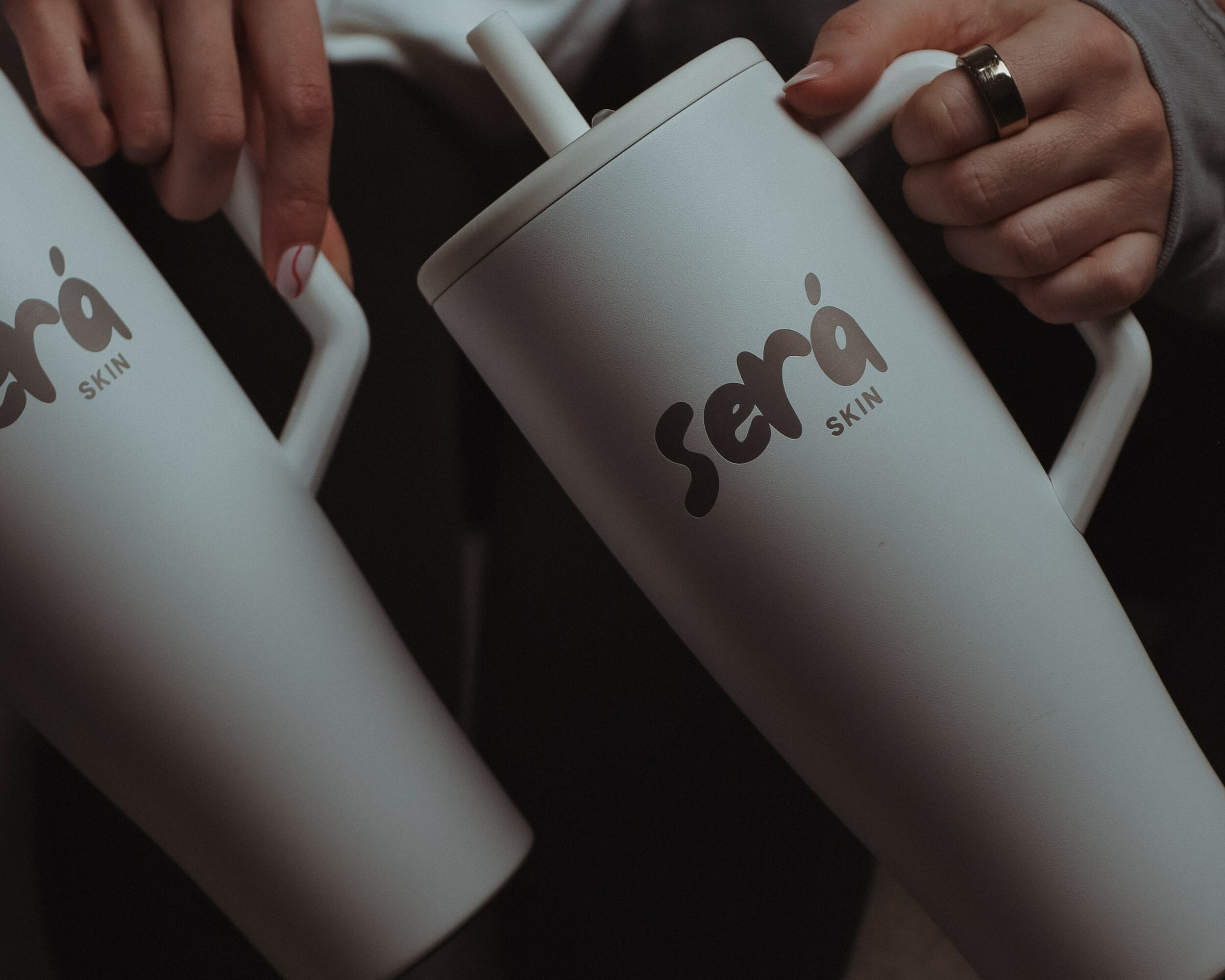 Two white containers with straws, one held by a person with a ring, labeled 'Serra Skin'.