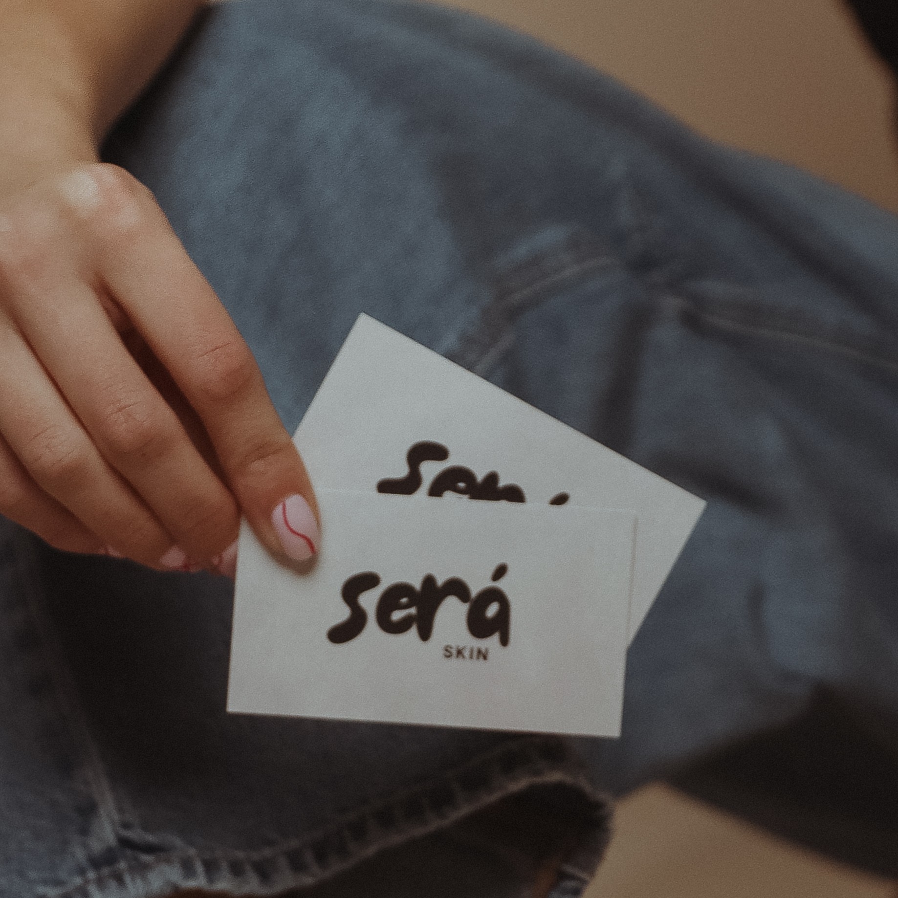 Person holding two white cards with handwritten text, sitting on a person's lap wearing jeans.