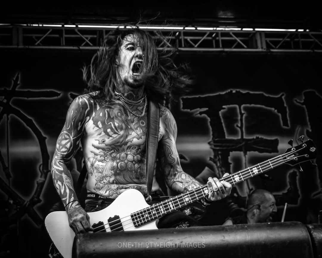 Musician with tattoos playing guitar on stage, hair flying, intense expression, black and white photo.