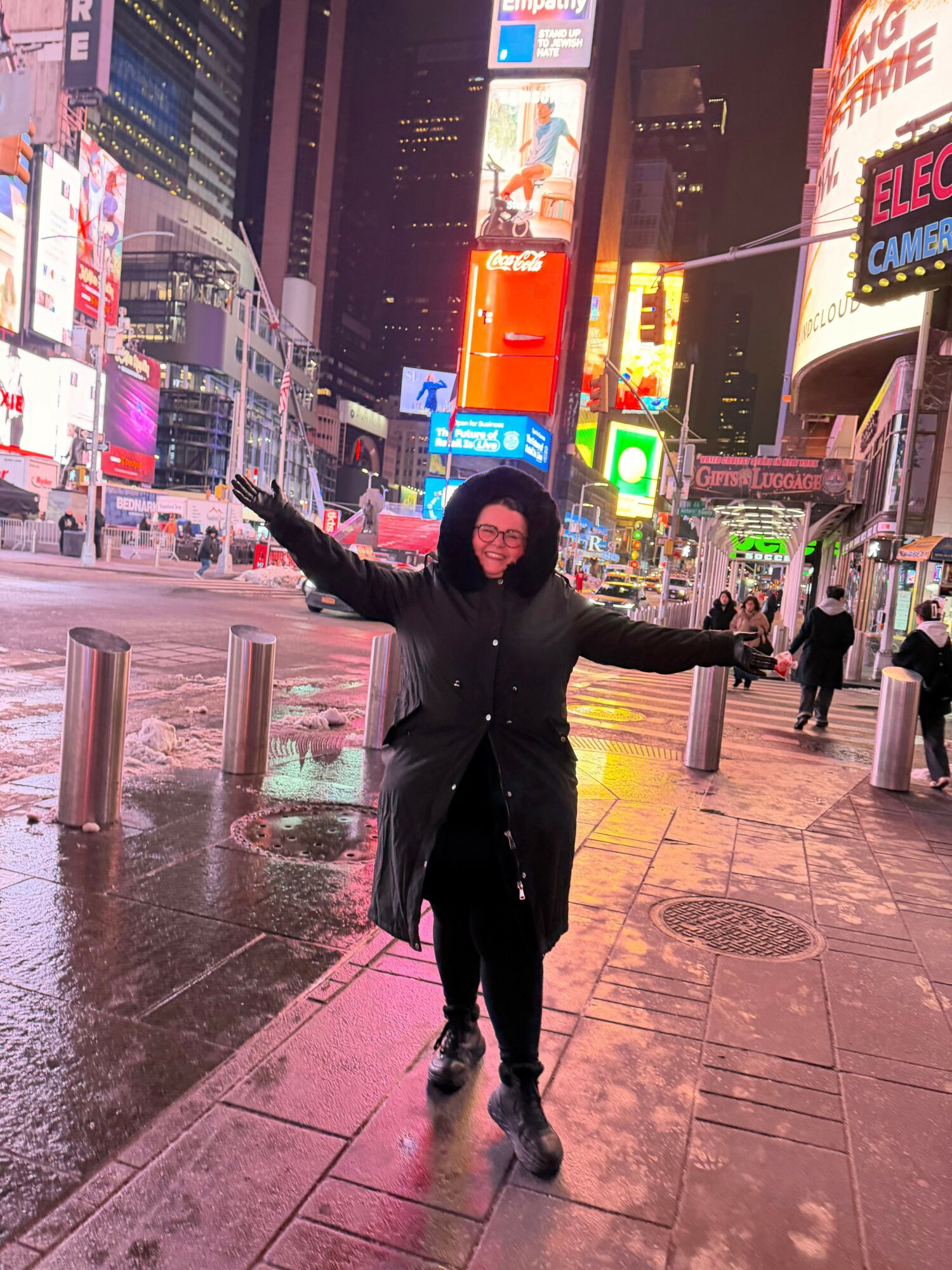 Person standing on wet city sidewalk at night, arms outstretched, illuminated by colorful neon signs and city lights.