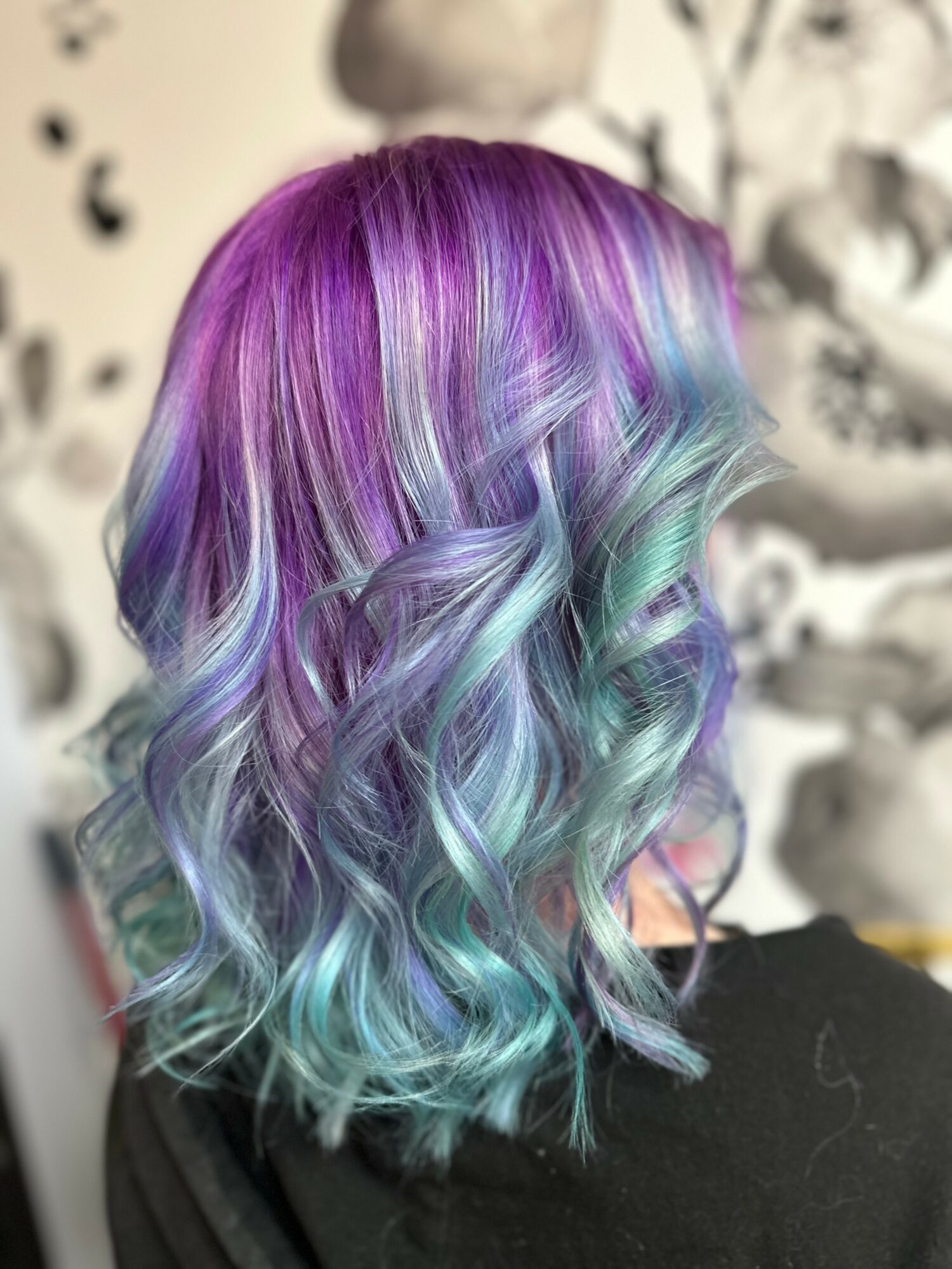 Person with wavy, multicolored hair in purple, blue, and green shades, styled in loose curls.