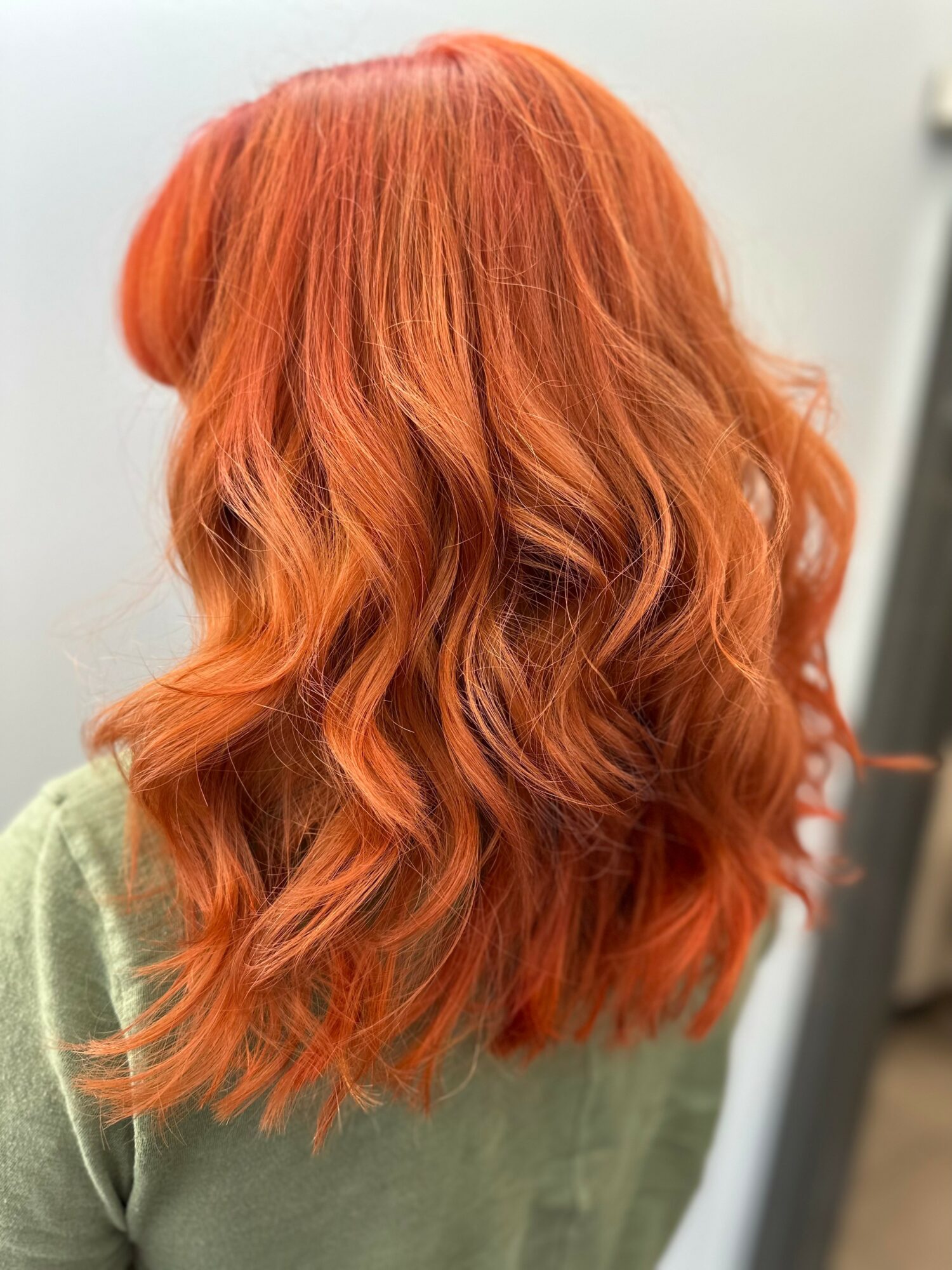 Person with long, wavy, orange hair seen from the back, wearing a green top.