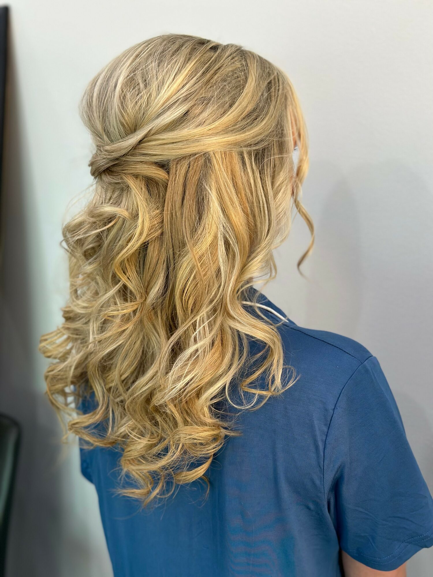 Side view of a woman with long, wavy blonde hair styled in loose curls, wearing a blue shirt.