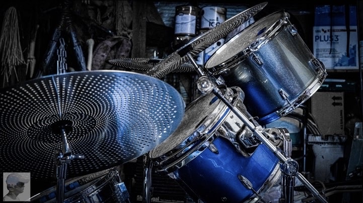 A drum set with blue drums and cymbals in a dark room, with various objects in the background.