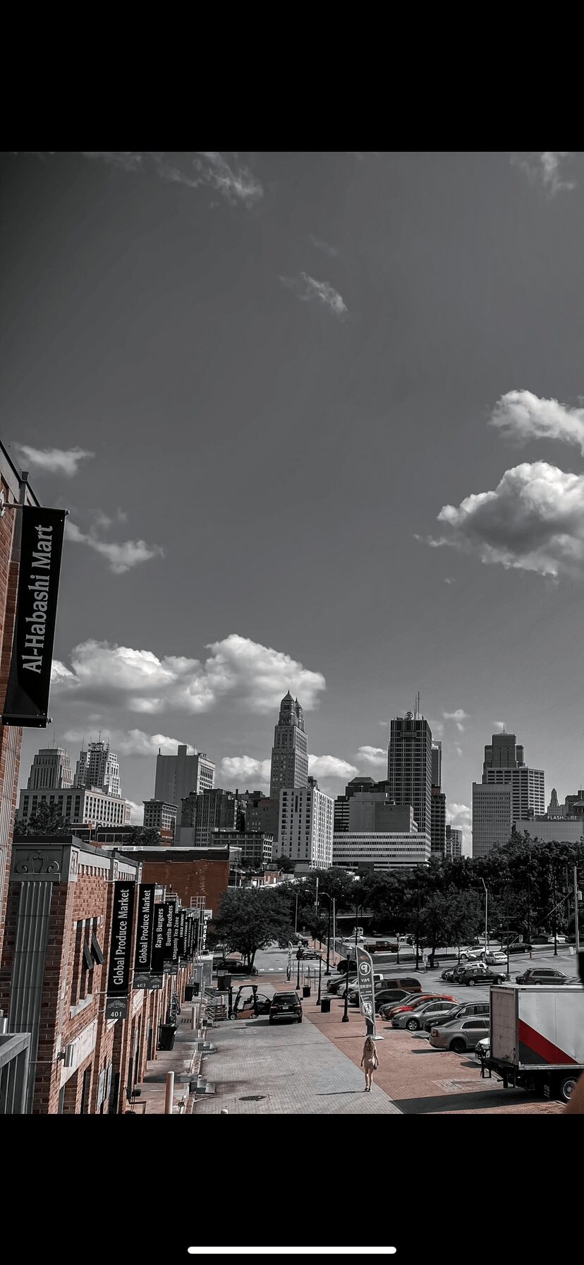 City skyline with tall buildings, parking lot, and partly cloudy sky, in black and white.
