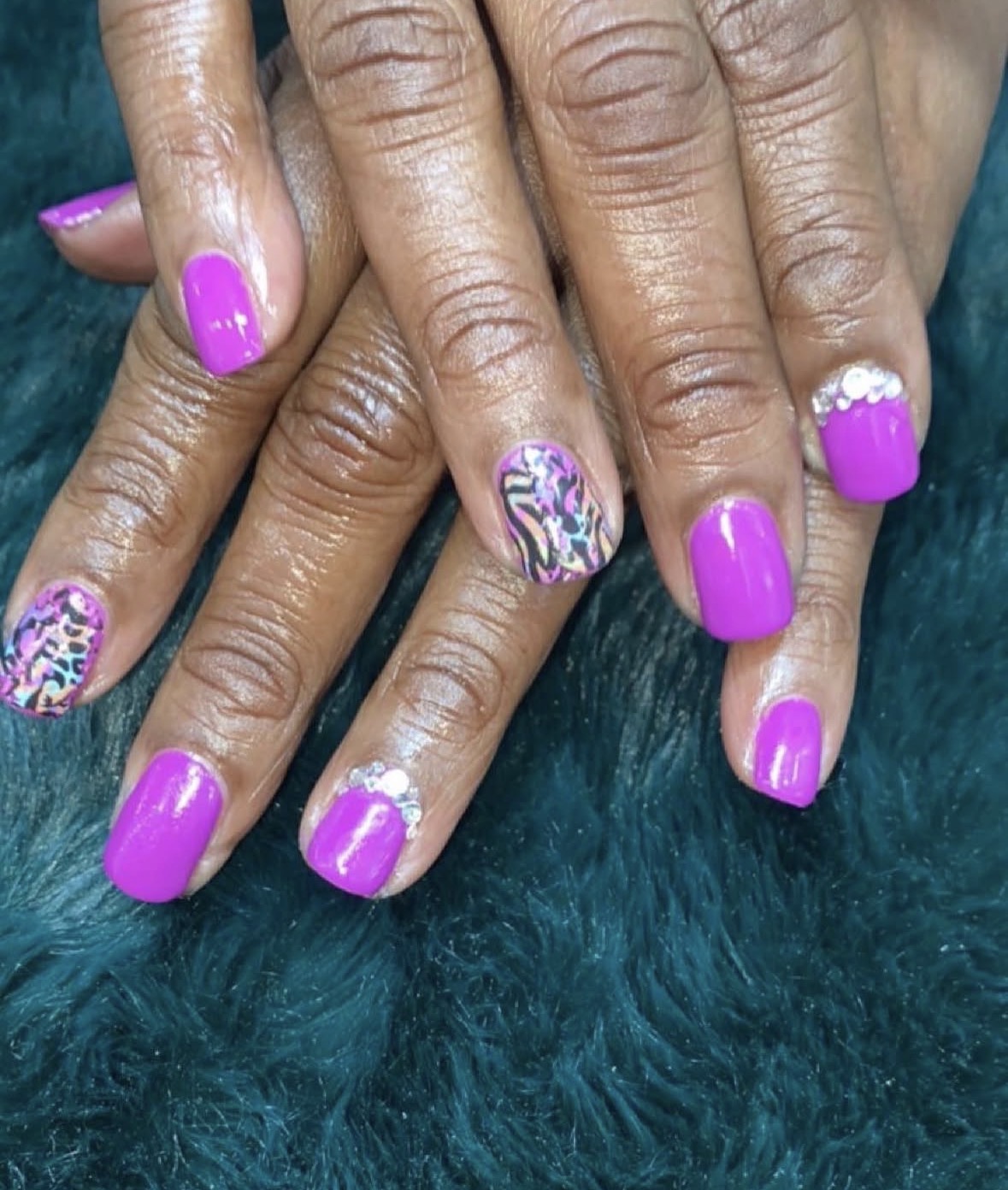 Hands with purple and patterned nail polish resting on a dark green surface.