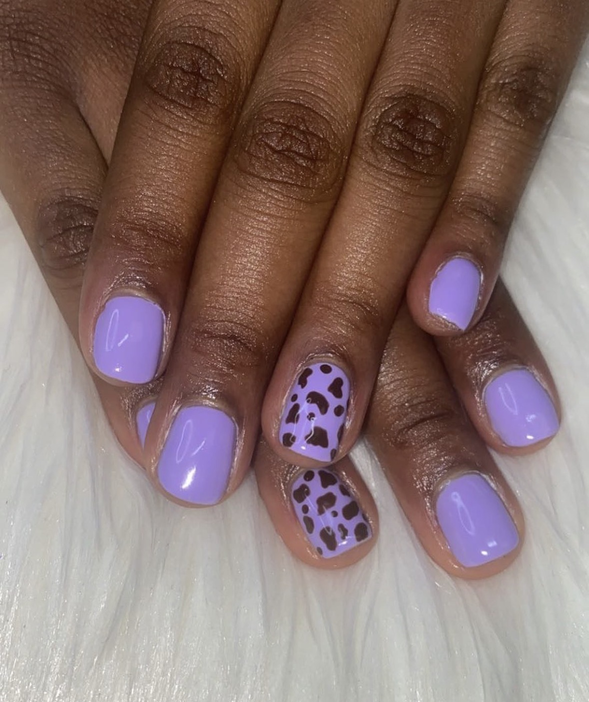 Hands with lavender nail polish and leopard print accent nails, resting on white fur surface.