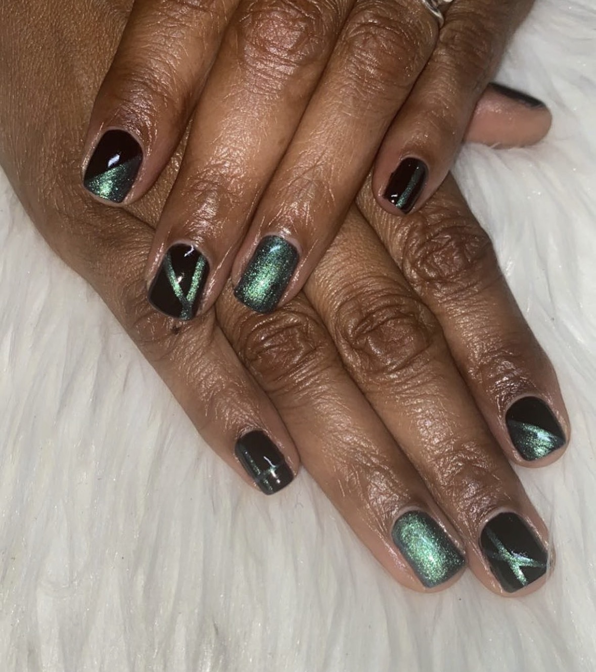 Hands with manicured nails painted black and green, with geometric designs, resting on a white surface.