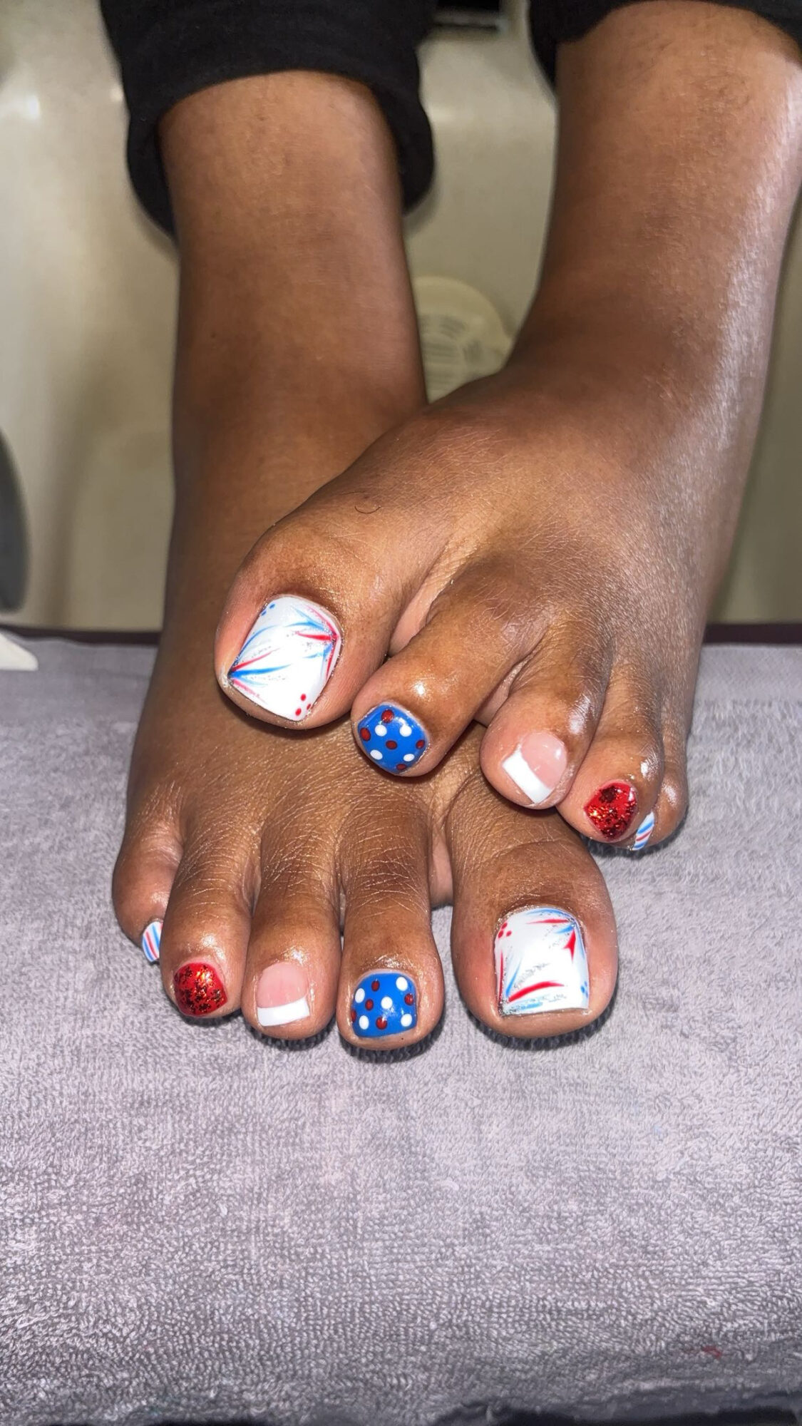 Feet with decorated toenails, some painted with red, blue, and white designs, resting on a surface.