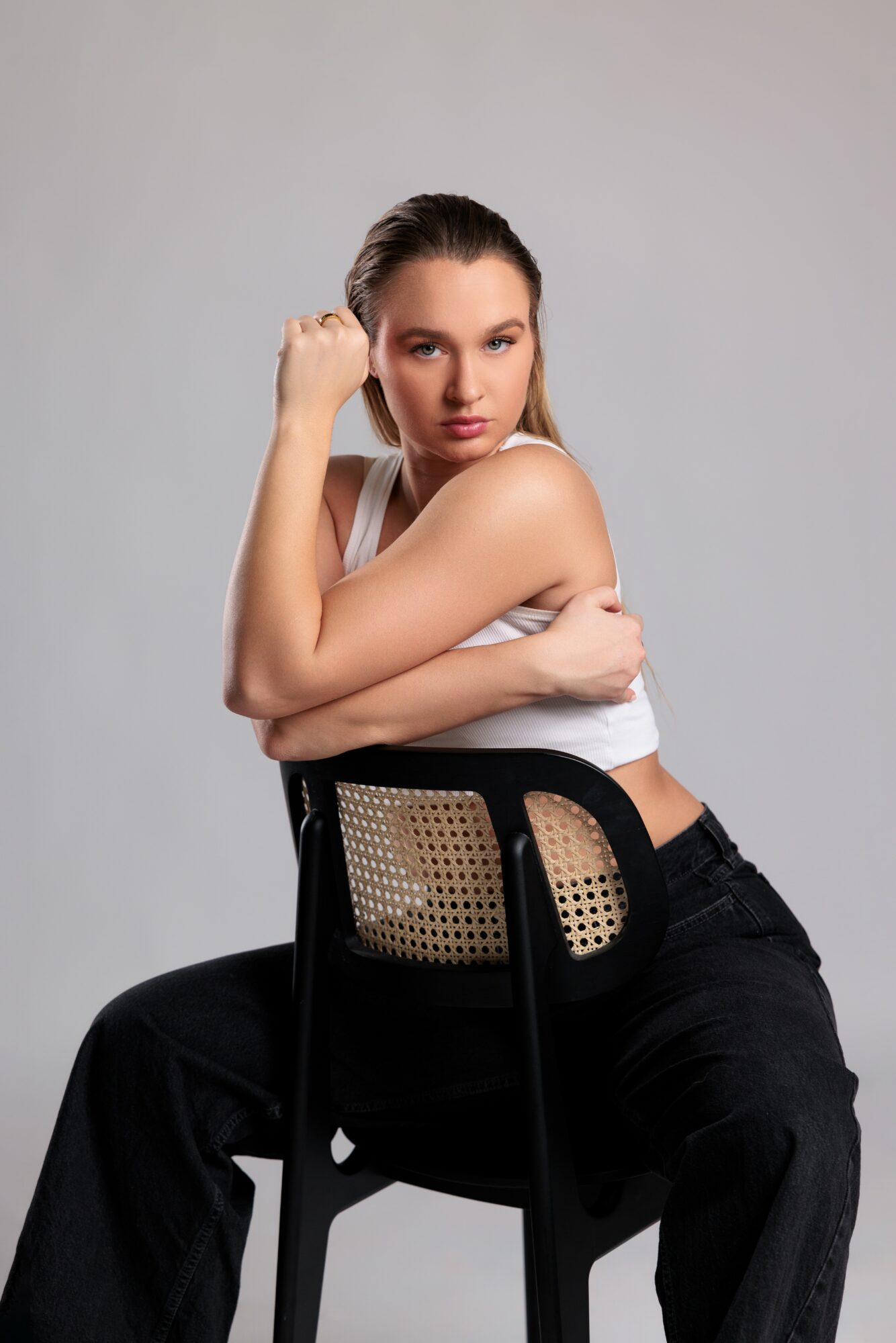 Young woman with long hair sitting on a chair, arms crossed, looking at the camera, gray background.