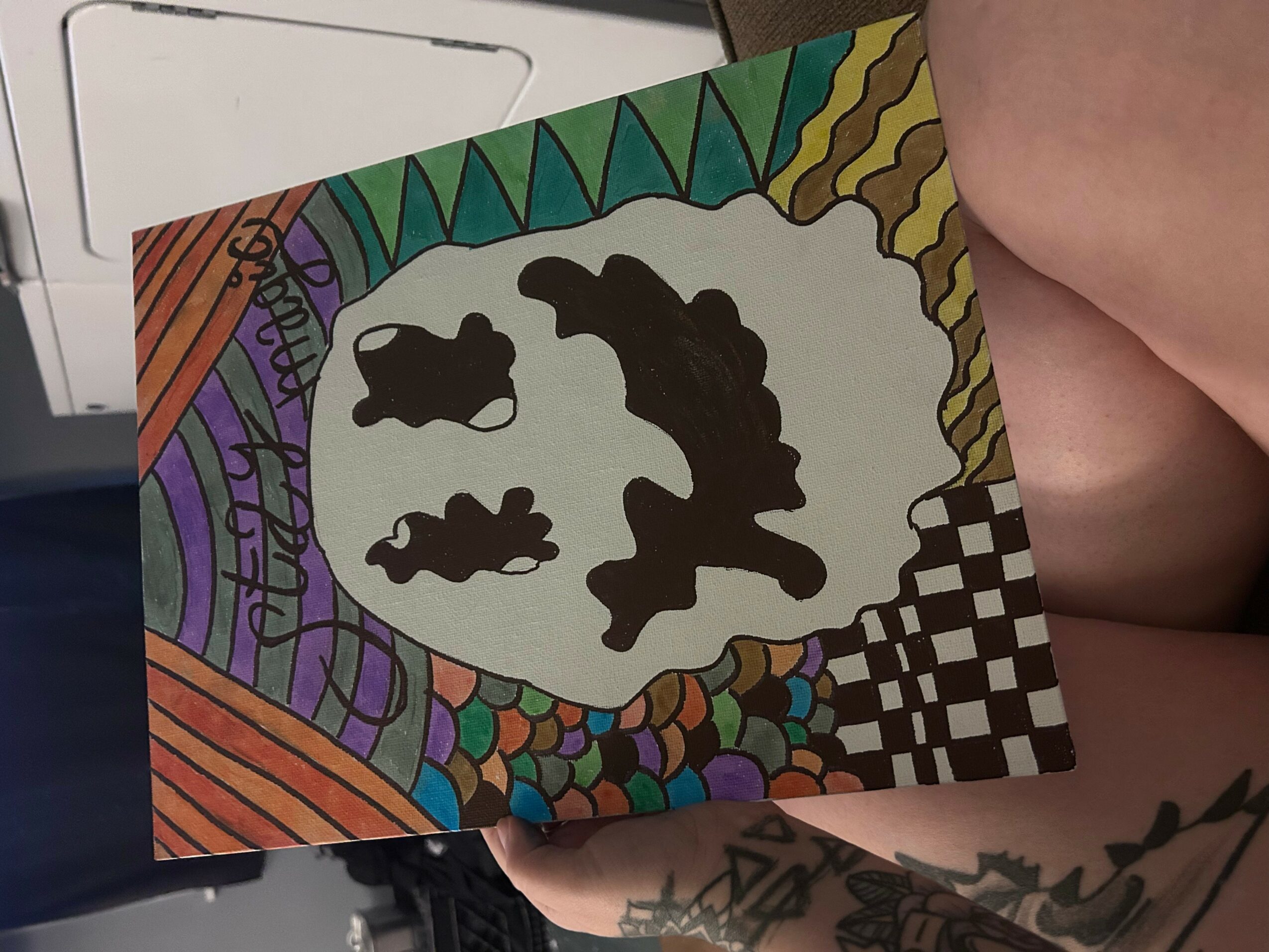 Colorful abstract drawing with black shapes inside a white oval, surrounded by rainbow colors and patterns, and a checkered area.