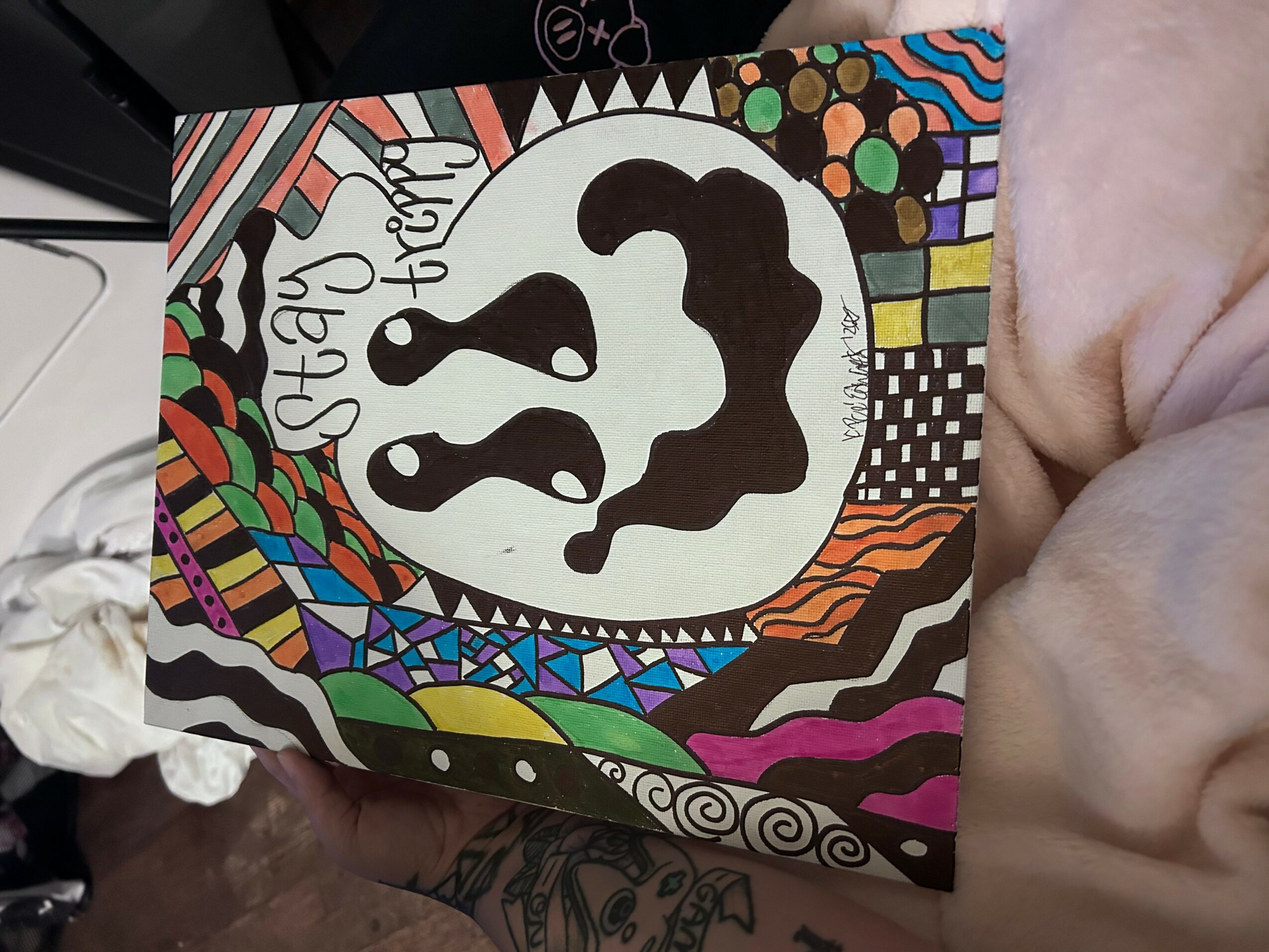 Colorful abstract drawing with a central black and white face, surrounded by vibrant patterns and shapes.