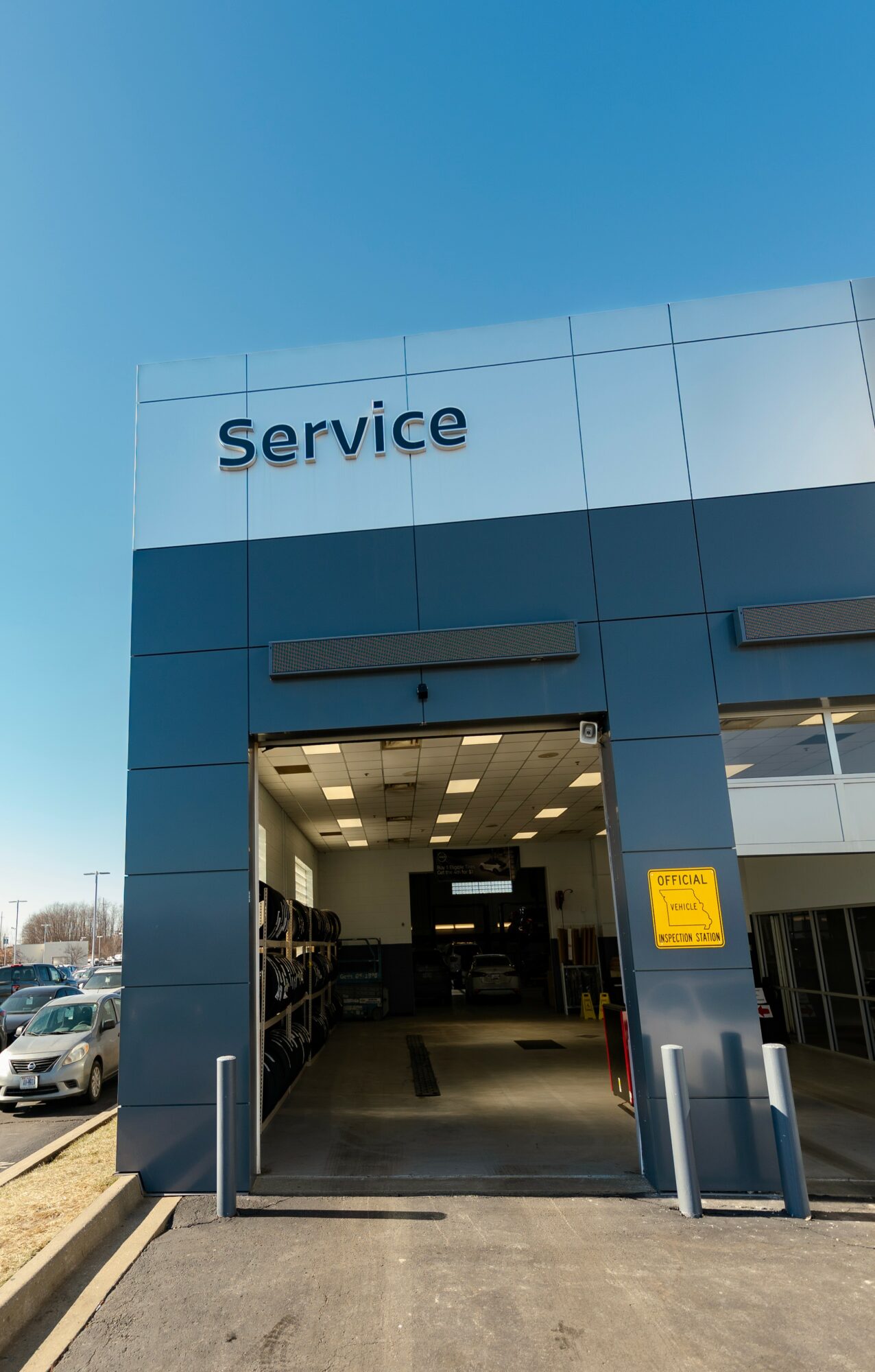 Open service entrance with cars parked outside, blue sky, and a yellow sign on the wall.