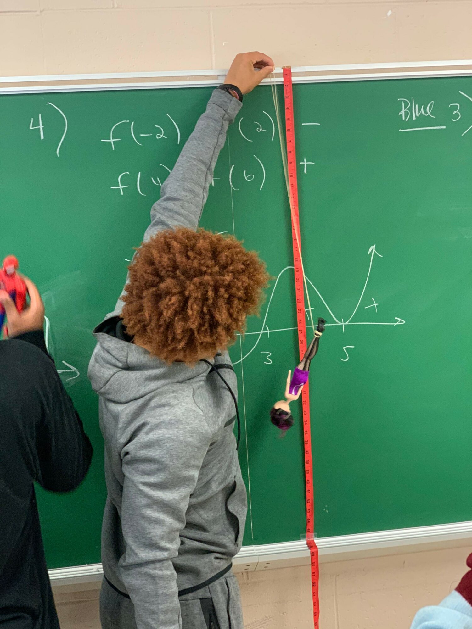 Person with curly hair pointing at a blackboard with a graph and equations, holding a red string across the board.