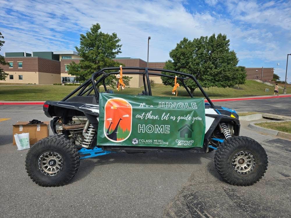 Off-road vehicle with a large sign on the side, parked on a street with trees and buildings in the background.