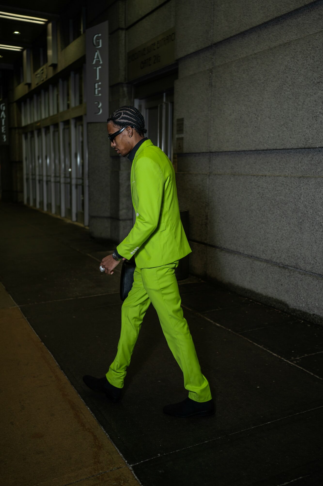 Person in bright green suit walking on sidewalk at night, near a gate and building wall.