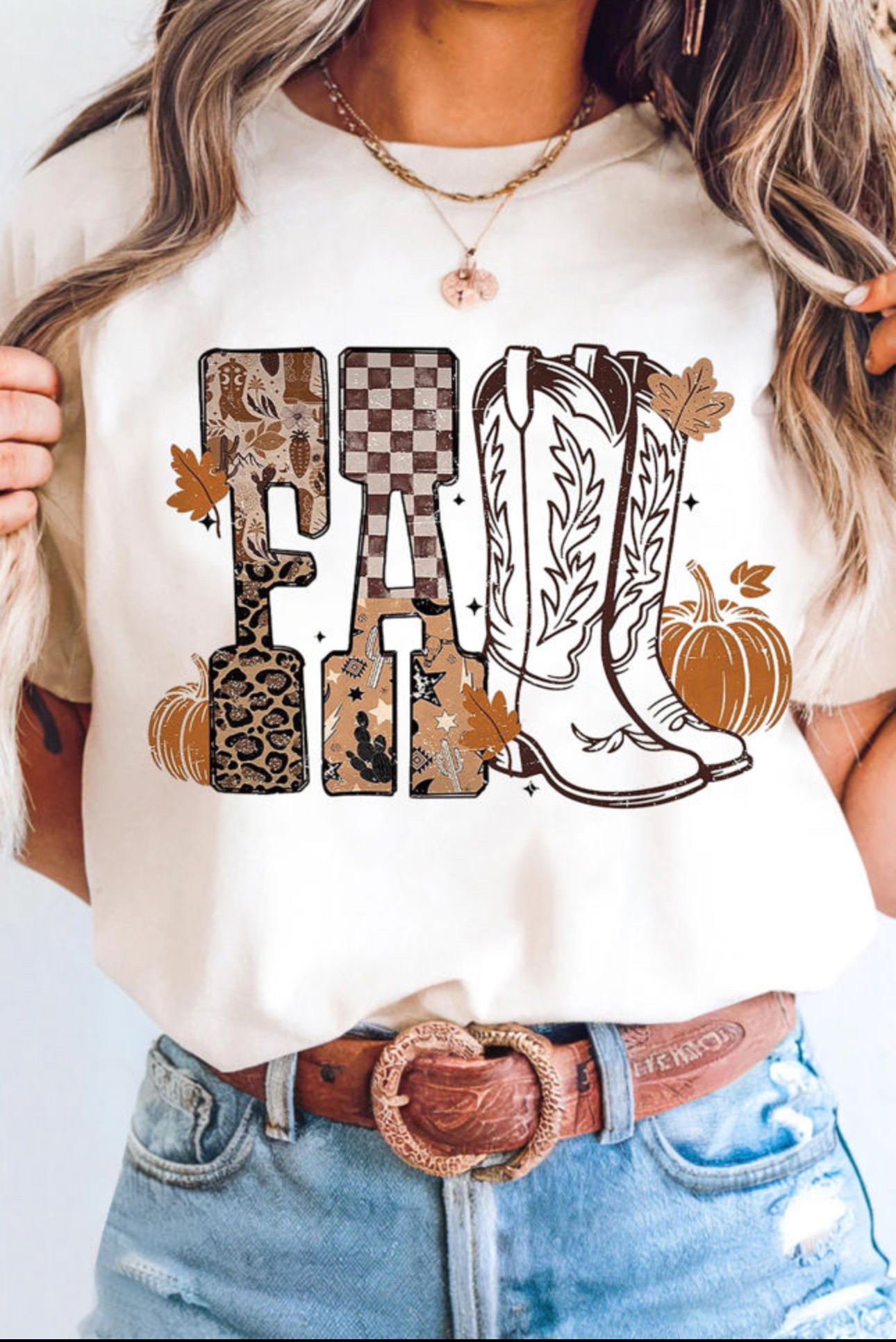 Person wearing a white shirt with fall-themed graphics, including pumpkins, leaves, and boots, and a necklace. Word 'FALL' is on the shirt.
