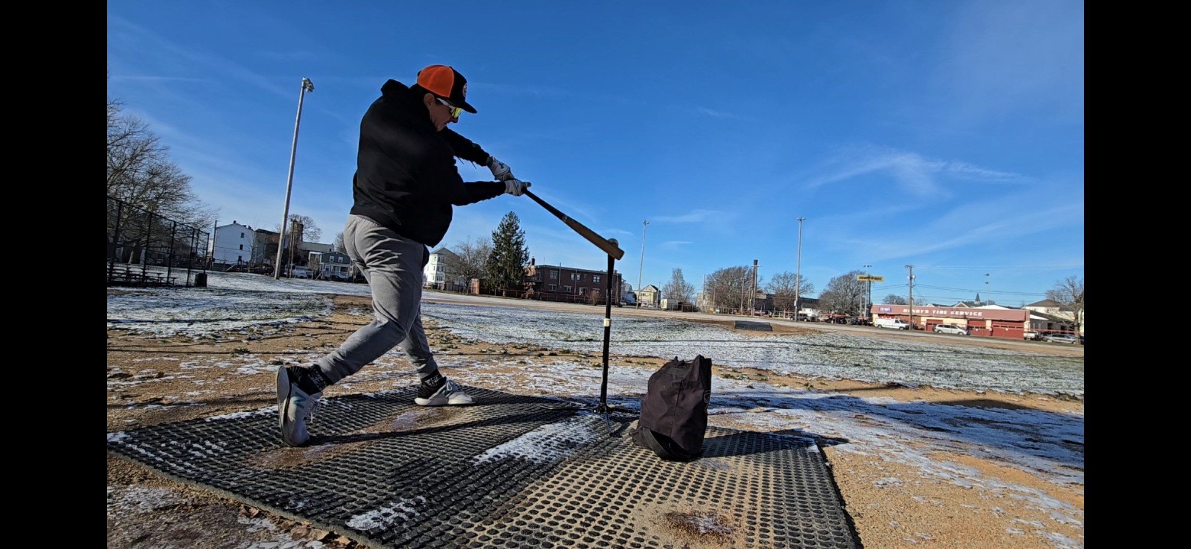 Person wearing an orange hat and dark clothing walks on a metal platform outdoors under a blue sky.