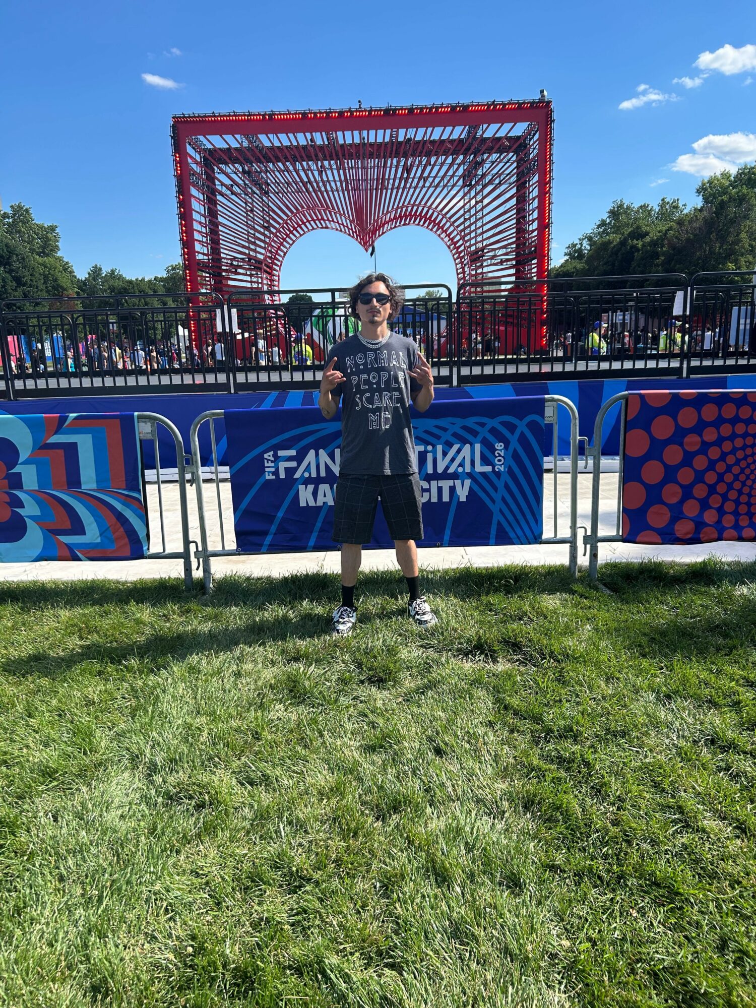 Person standing in front of a colorful festival entrance with a heart-shaped arch, blue sky, and trees in background.