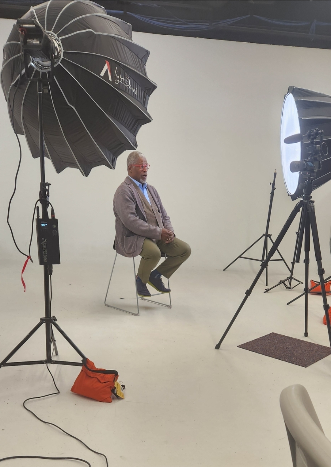 Man sitting on a chair in a photography studio with lighting equipment around him.