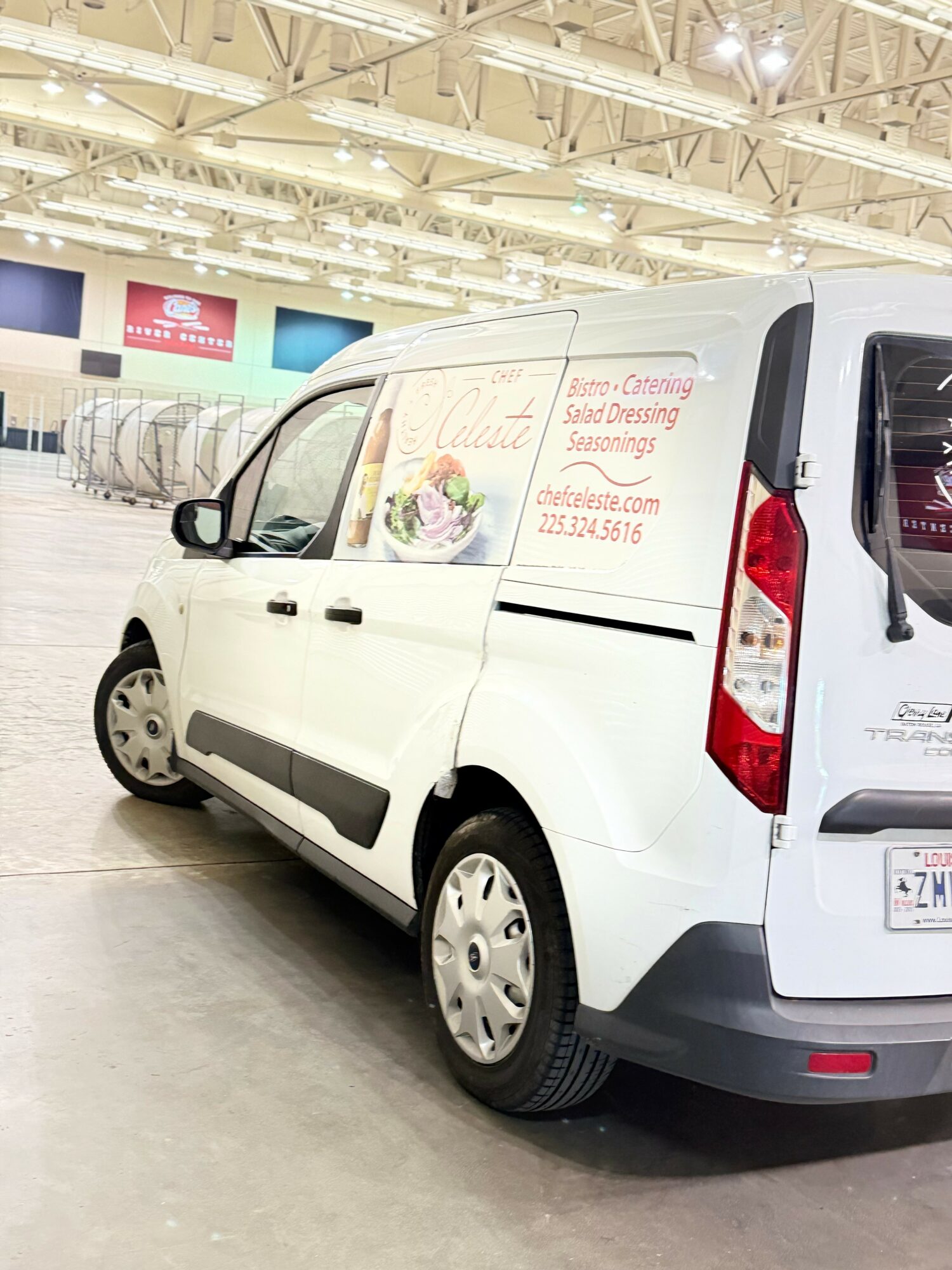 White van parked indoors with signage on the side, ceiling with lights, and shopping carts in the background.