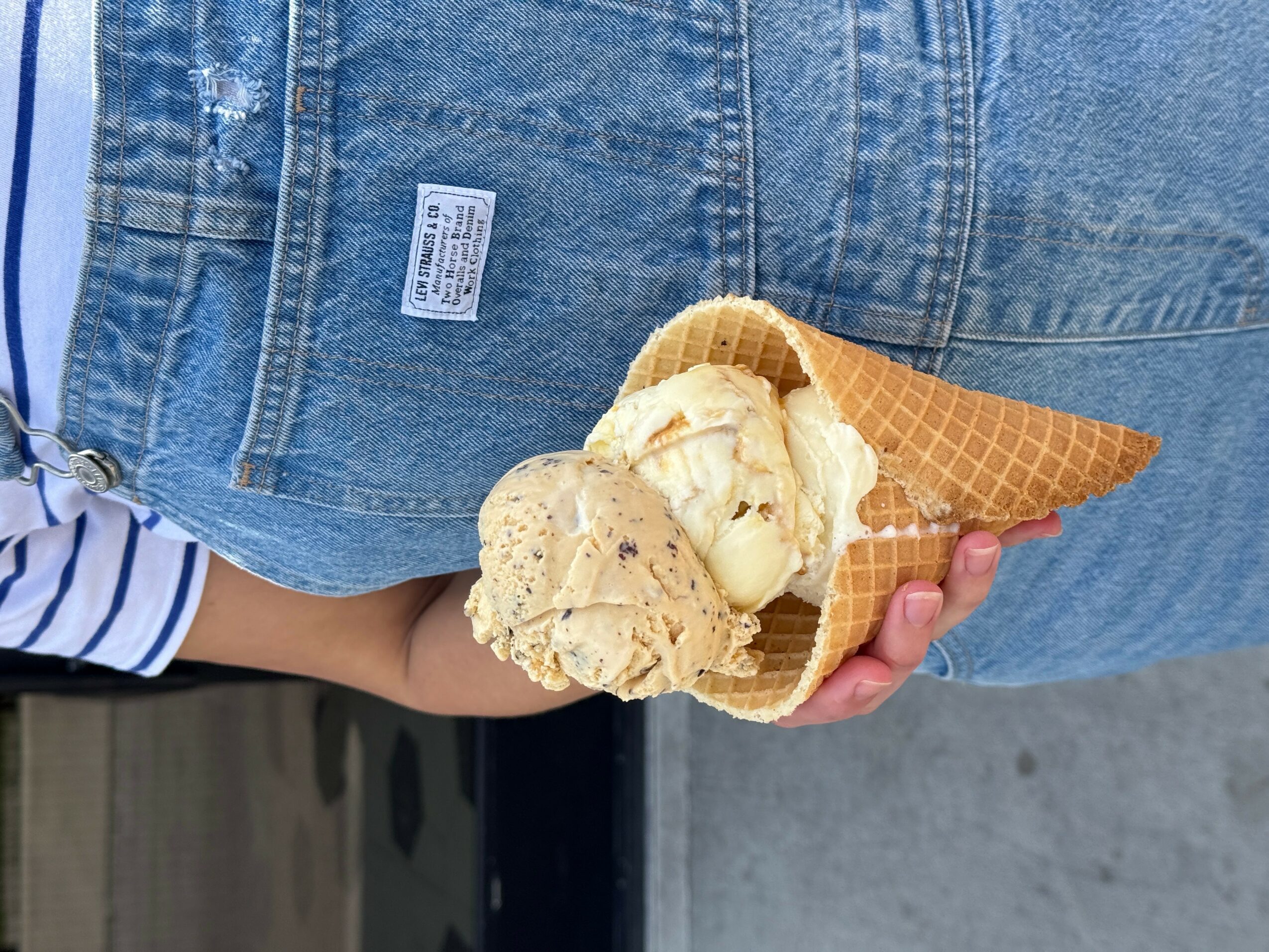 Child holding a cone with ice cream and cookies, wearing blue jeans and a striped shirt sleeve visible.