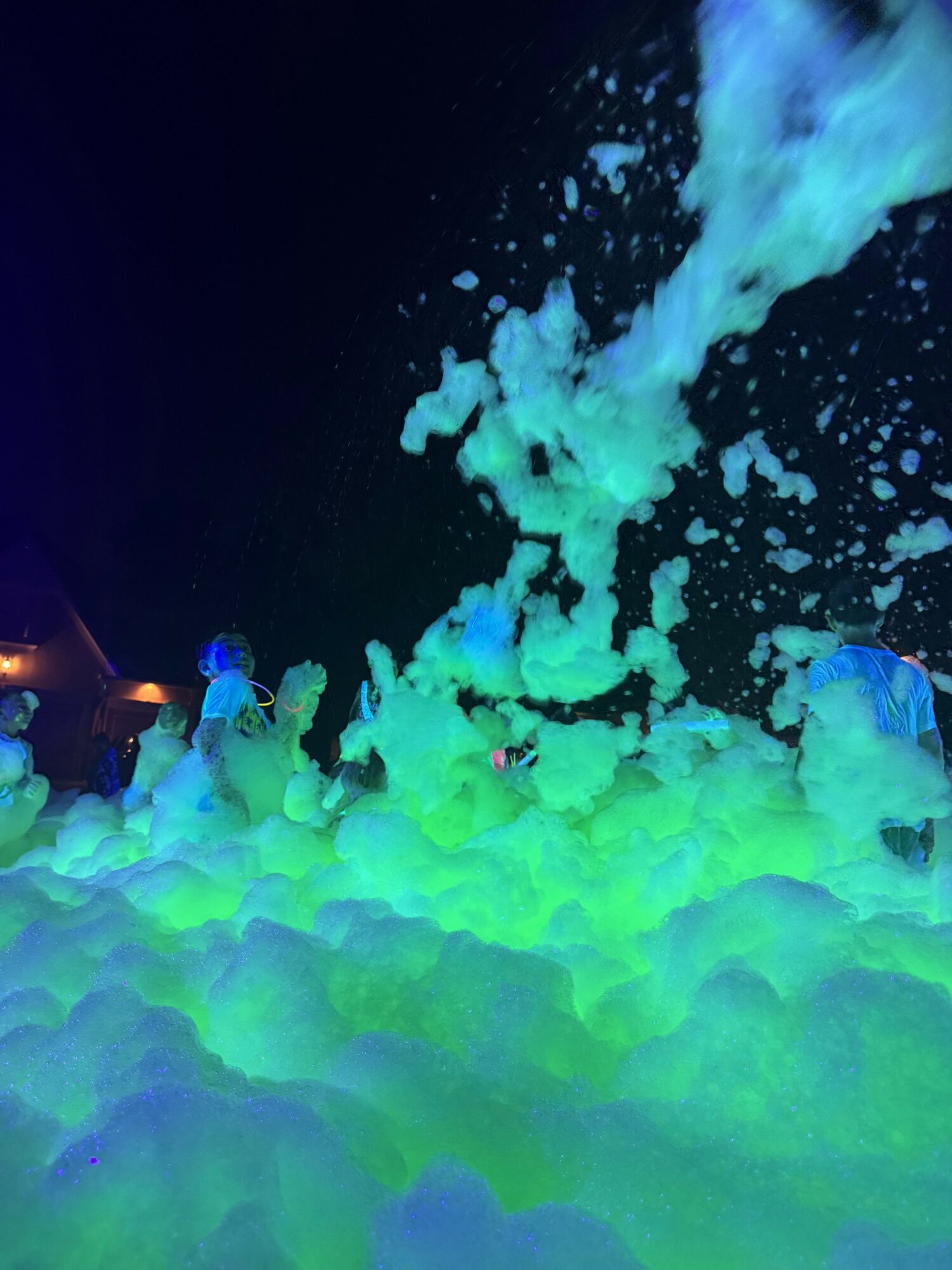 People in a foam party with glowing foam and colorful lights at night, splashing and dancing.