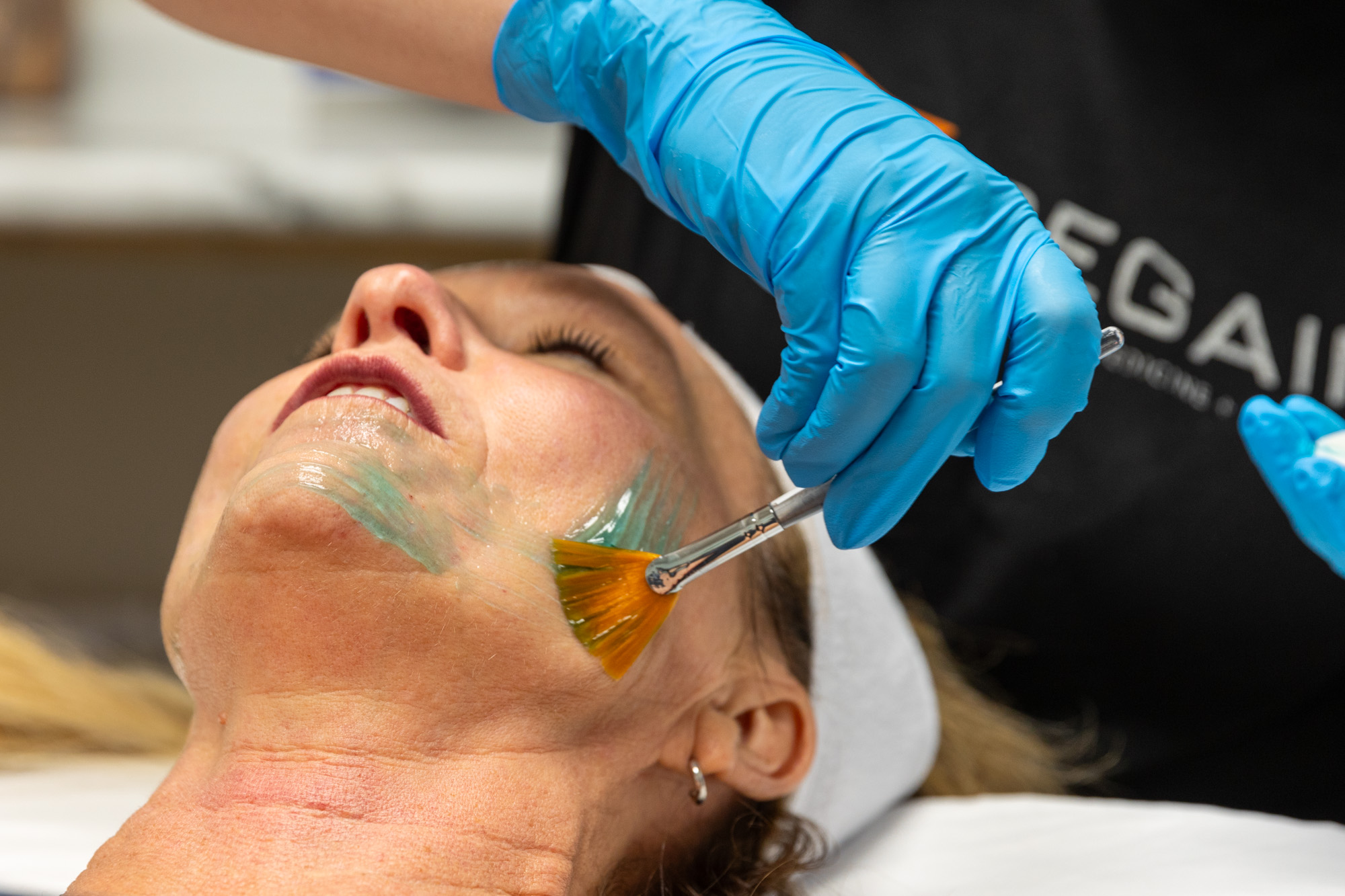 Person receiving a facial treatment with a brush applied to their face, wearing a headband, in a clinical setting.