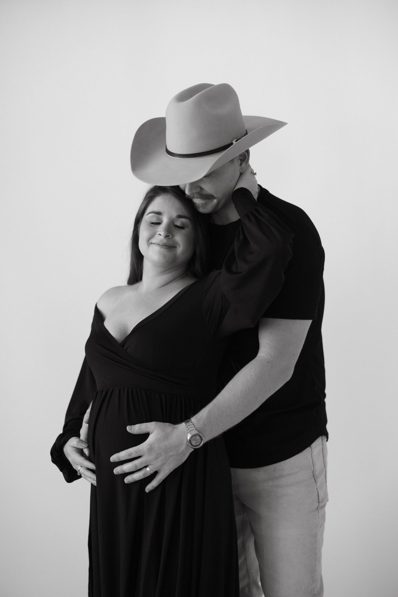 A couple, with the woman pregnant, standing close together, the man wearing a large hat, both smiling gently, black and white photo.