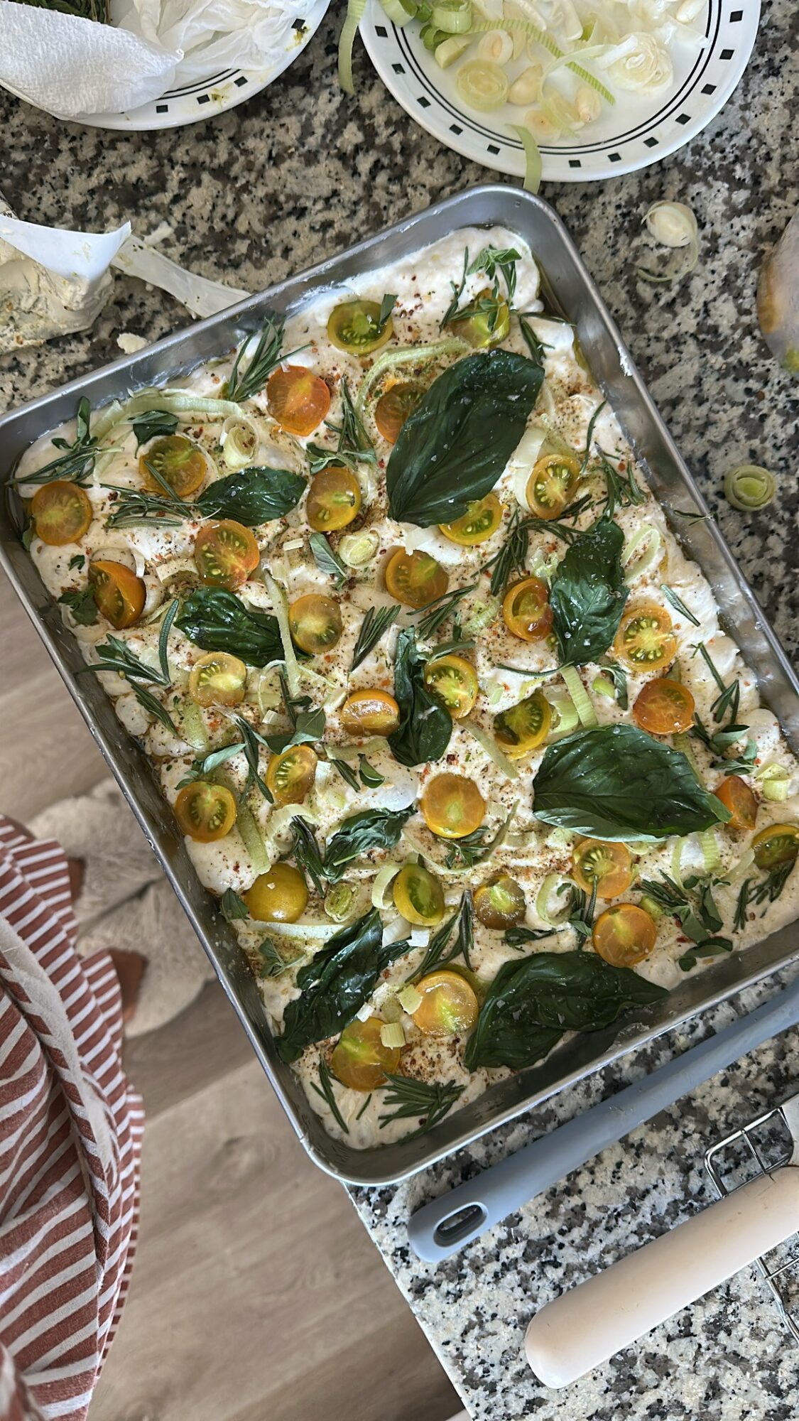Baked dish with cherry tomatoes, green leaves, and cheese in a metal tray on a granite countertop.