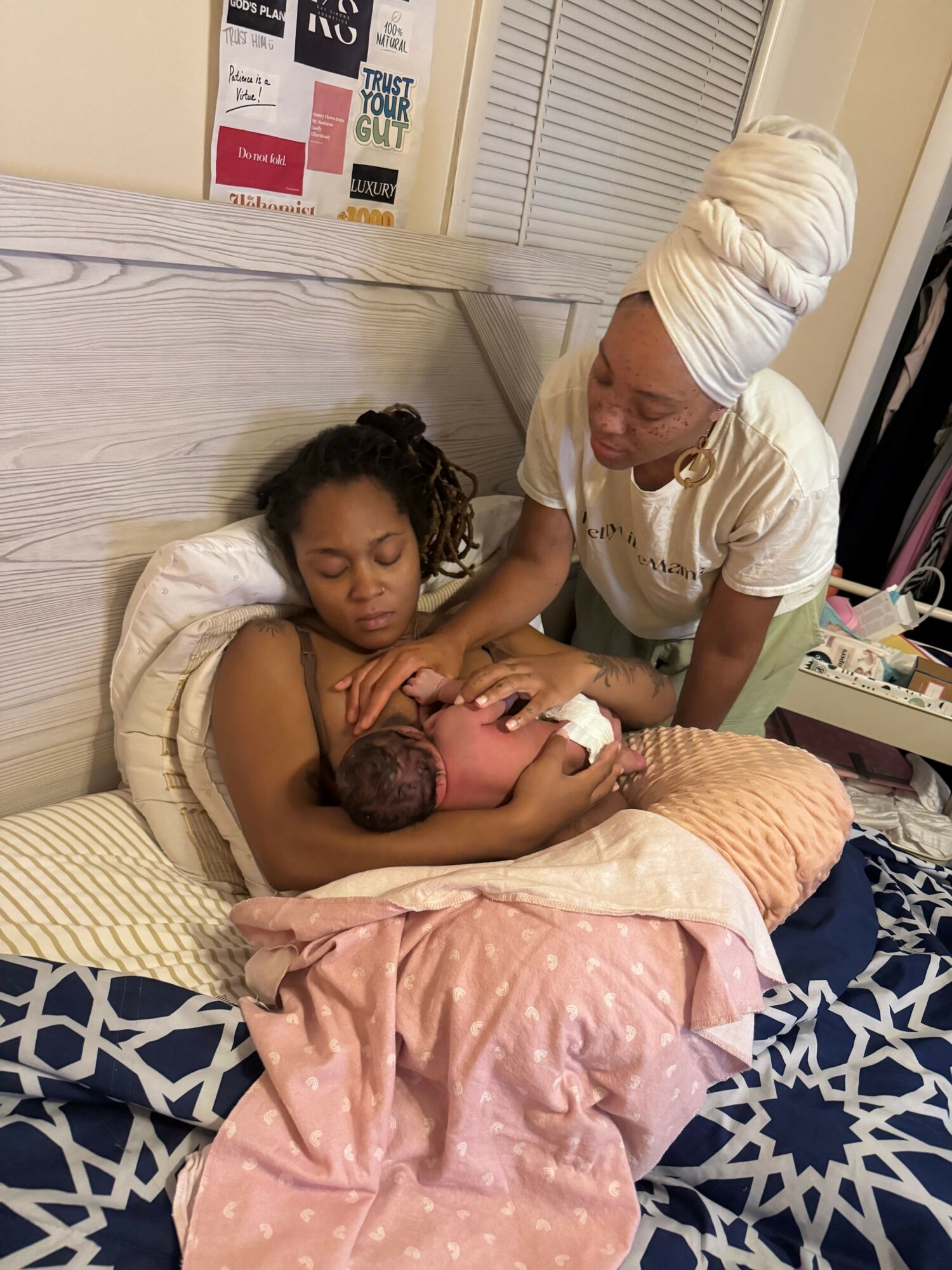 Two women and a baby on a bed, with one woman lying down and the other leaning over, holding the baby.