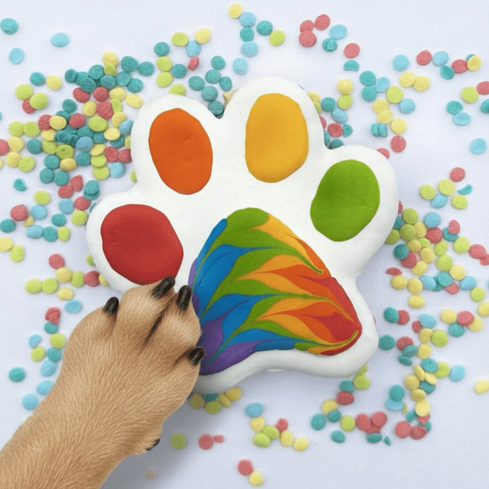 A paw-shaped cookie with colorful paint, surrounded by multicolored sprinkles on a white background.