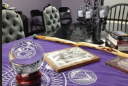 Table with a purple cloth, a crystal ball, a wooden staff, and books, surrounded by chairs and candles.