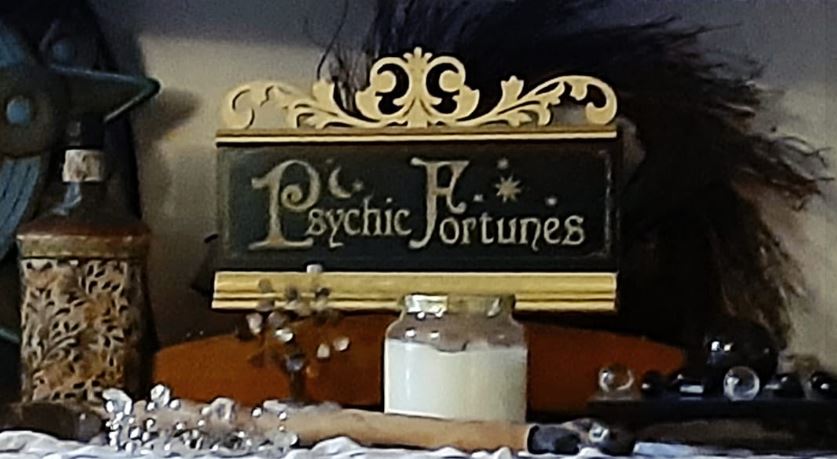Decorative sign reading 'Psychic Fortunes' with ornate gold design, placed on a table with various objects around it.