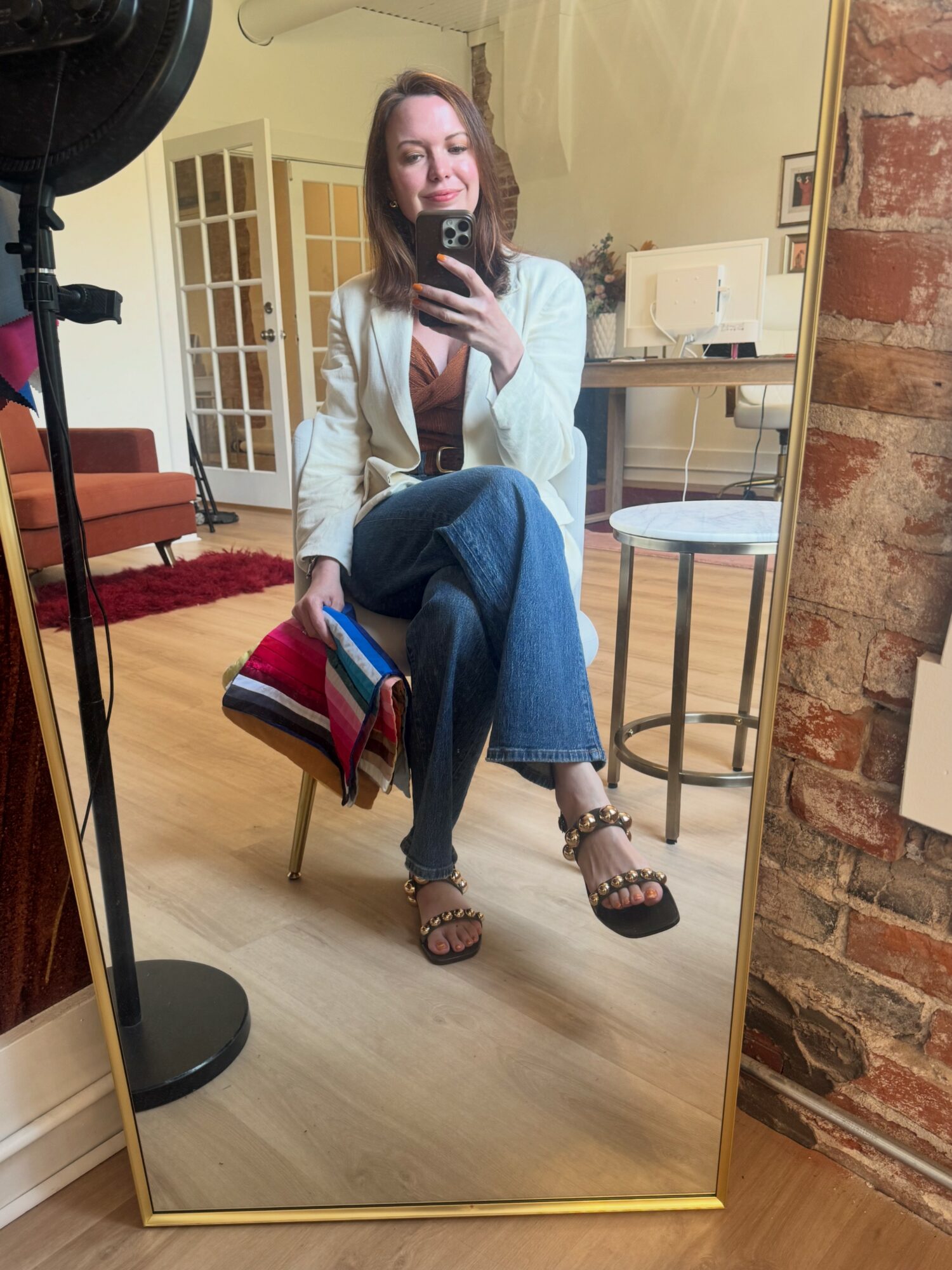 Woman sitting on a chair taking a mirror selfie in a room with a brick wall and wooden floor.