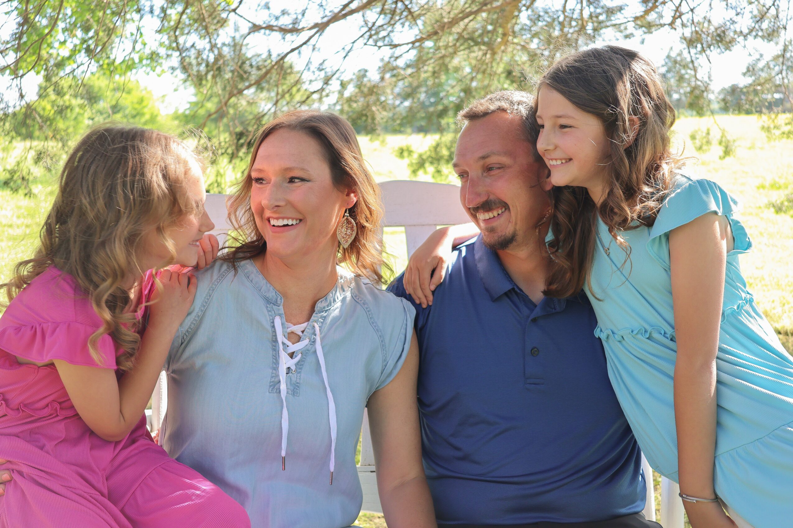 Family of four smiling outdoors, two adults and two children, enjoying a sunny day.