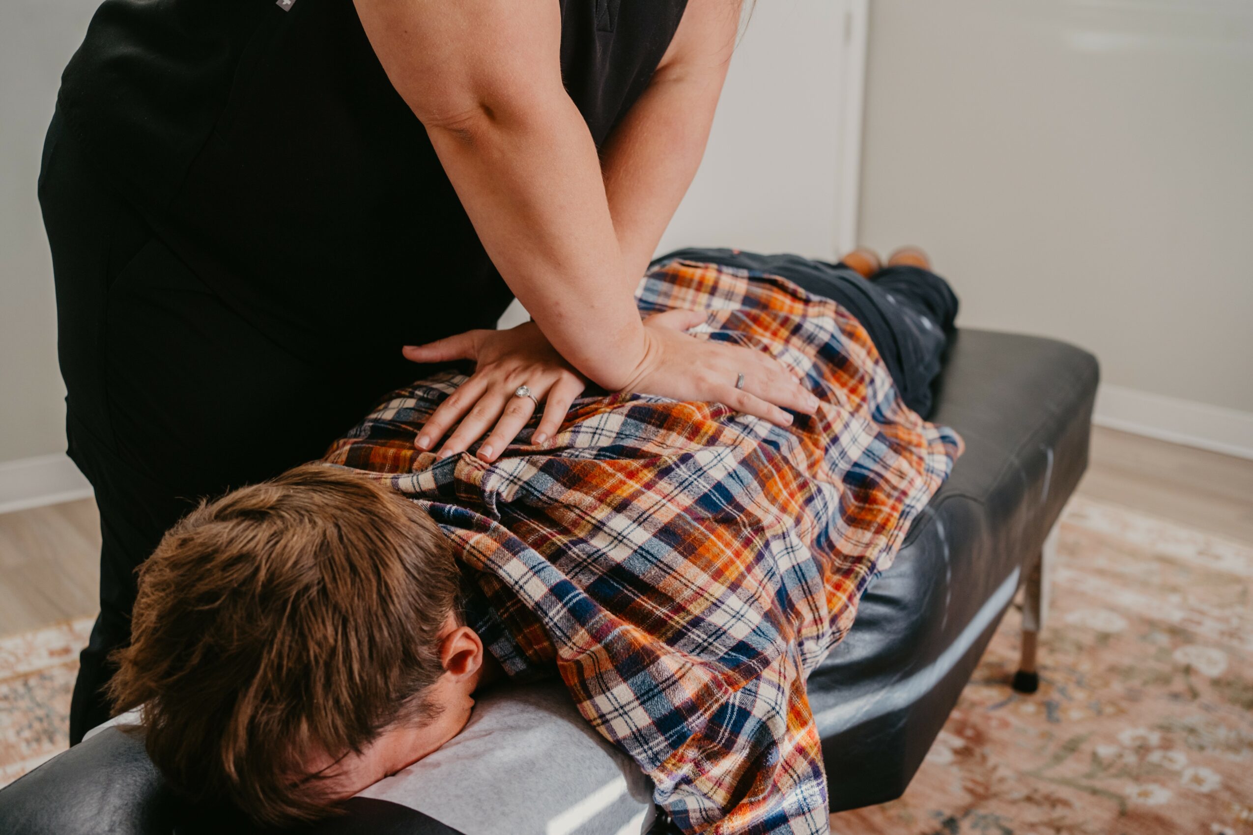 Person receiving a back massage from a massage therapist in a room with a rug and white walls.