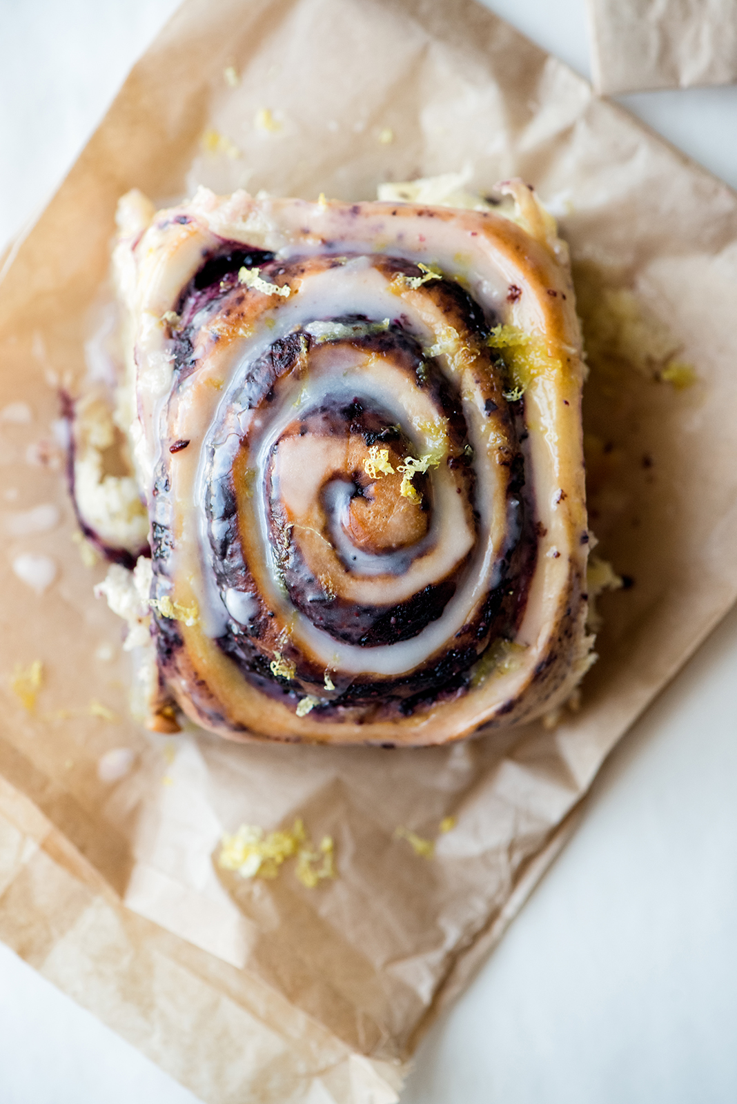 Swirled pastry with icing and lemon zest on parchment paper, viewed from above.