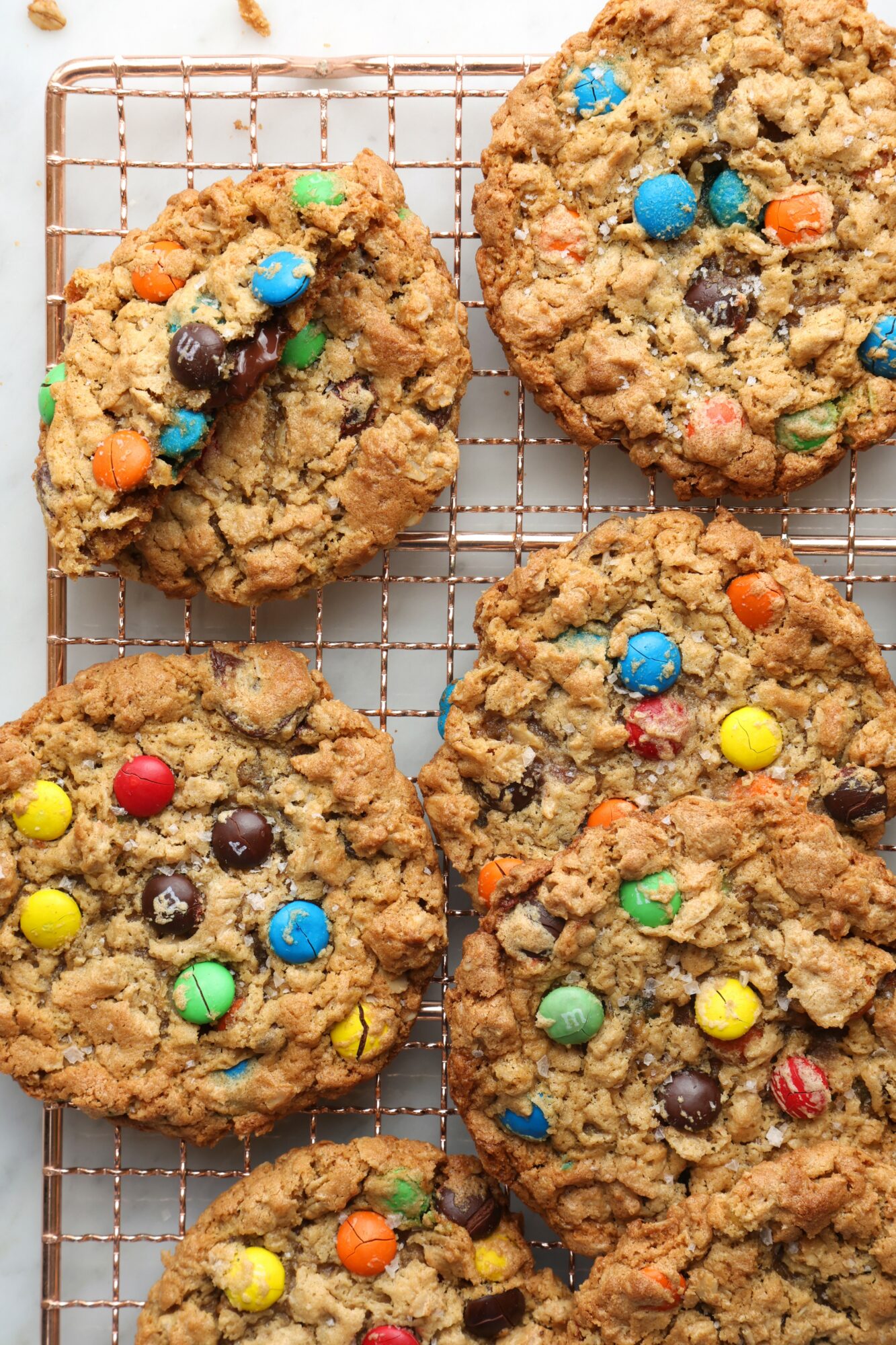 Six cookies with colorful candies on a wire cooling rack, some cookies overlapping each other.