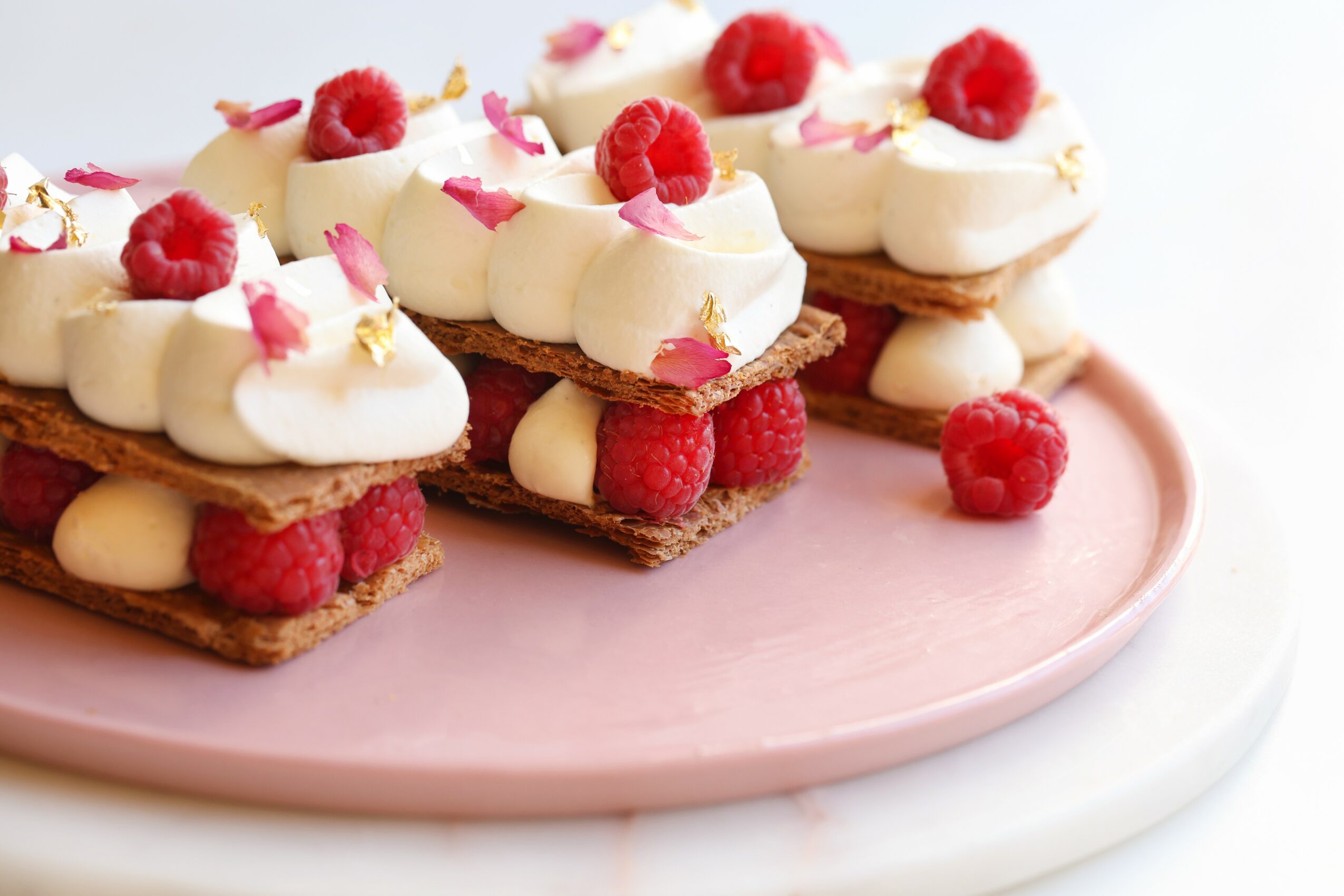 Dessert with cream, raspberries, and pink flower petals on a pink plate, close-up view.