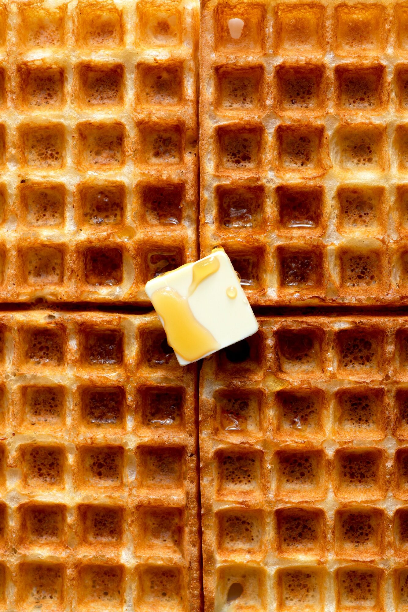 Close-up of four waffle pieces with a small piece of butter on top, arranged in a grid pattern.