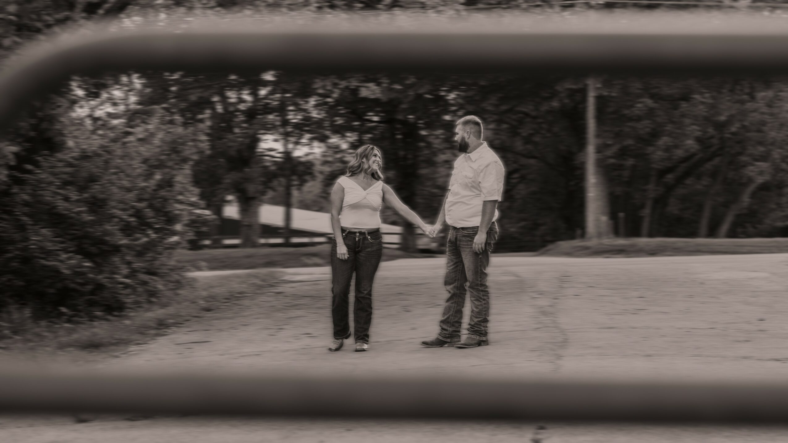 Two people holding hands and standing outdoors on a paved area, with trees in the background.
